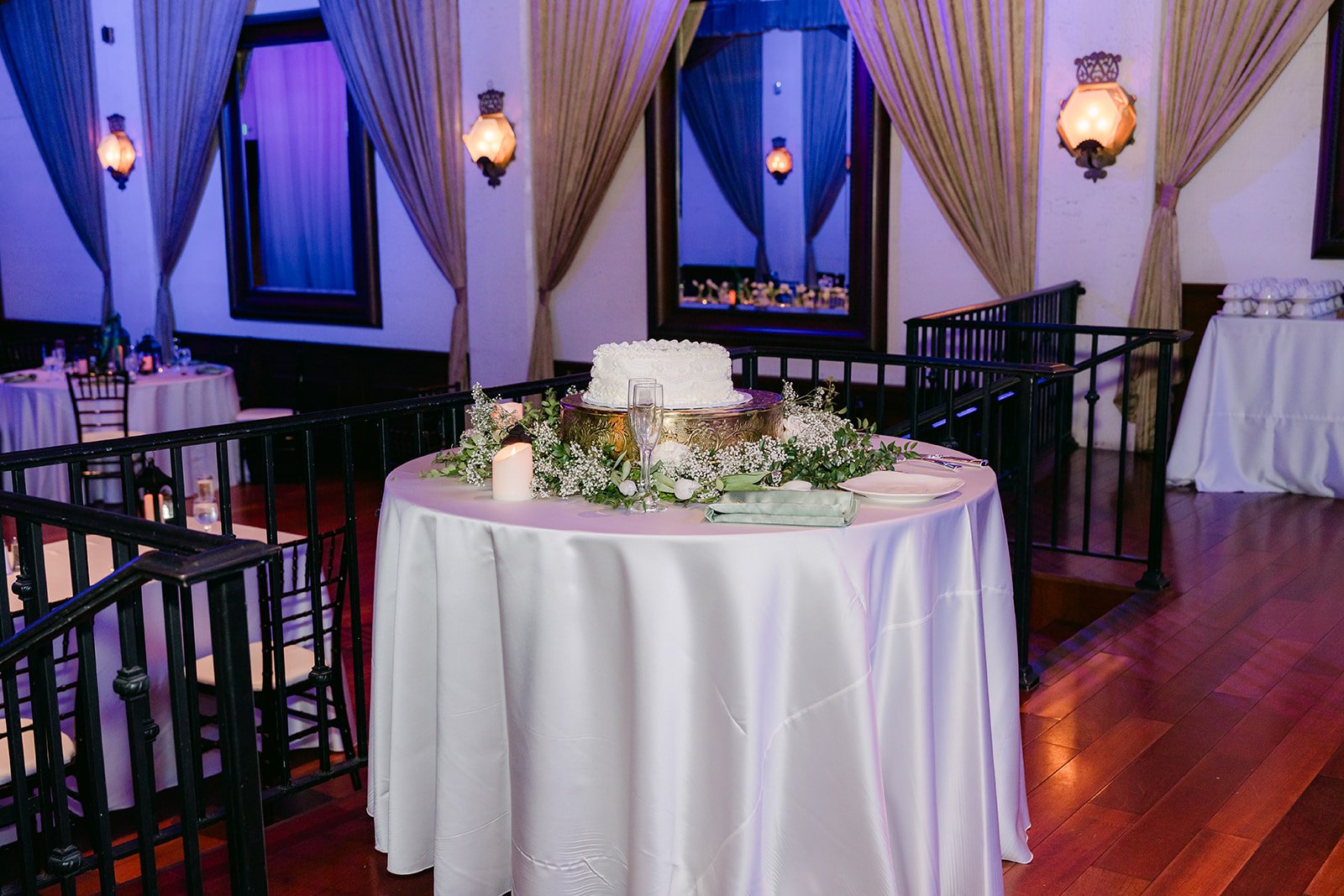 Heart shaped wedding cake on a greenery wrapped table in the reception room