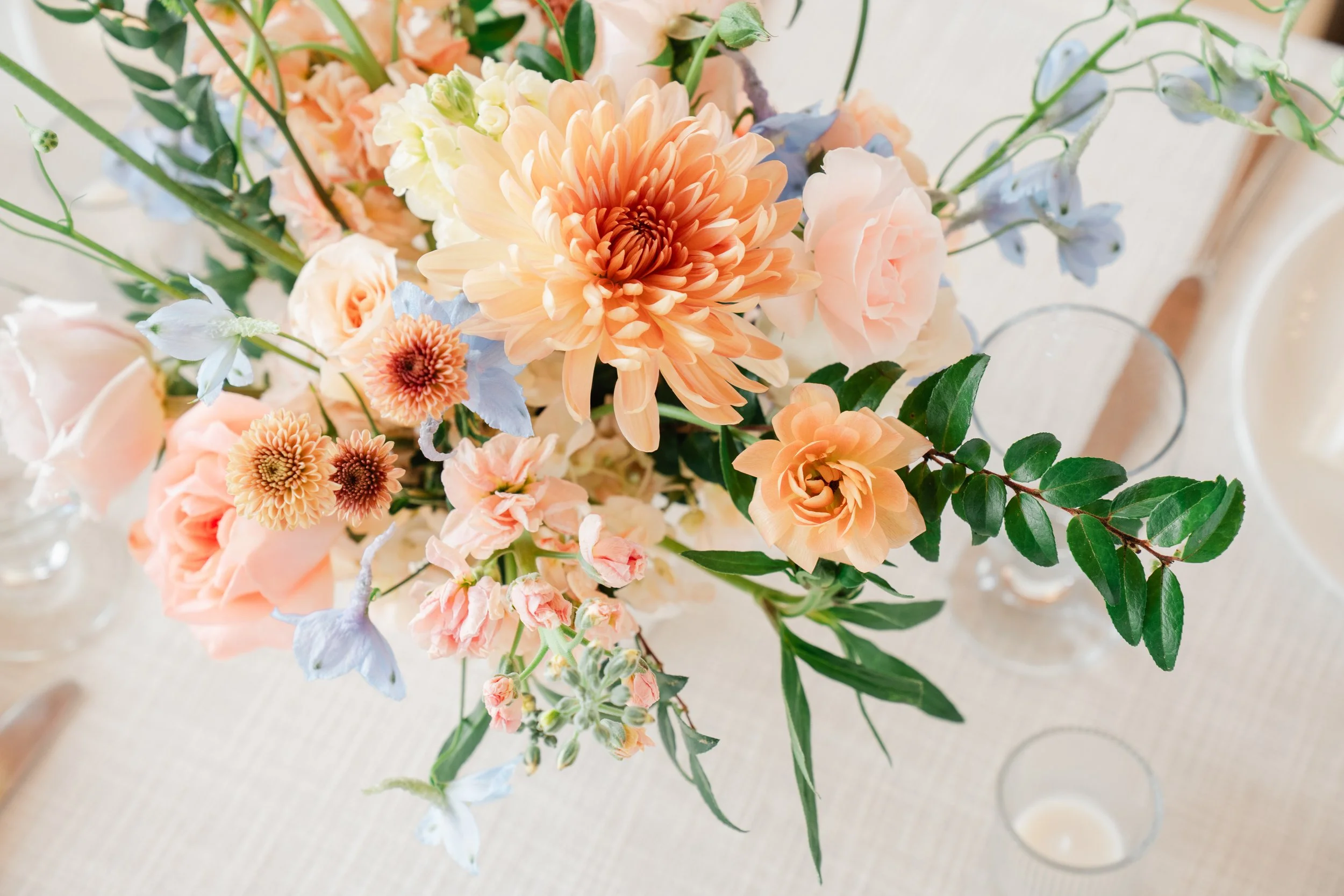 A bouquet of light peach, cream, and orange flowers with green leaves on a cream-colored table.
