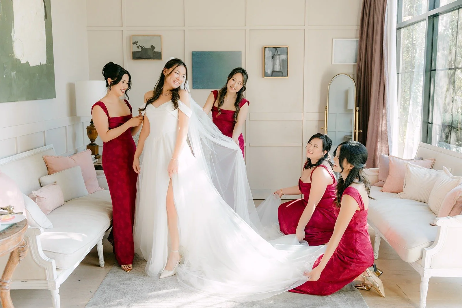 Bridesmaids in burgundy dresses fluffing Jadee's train