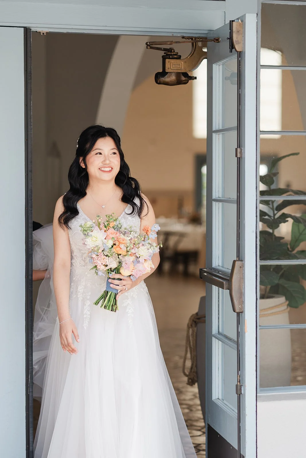 Constance stepping out through the blue doors with her bouquet
