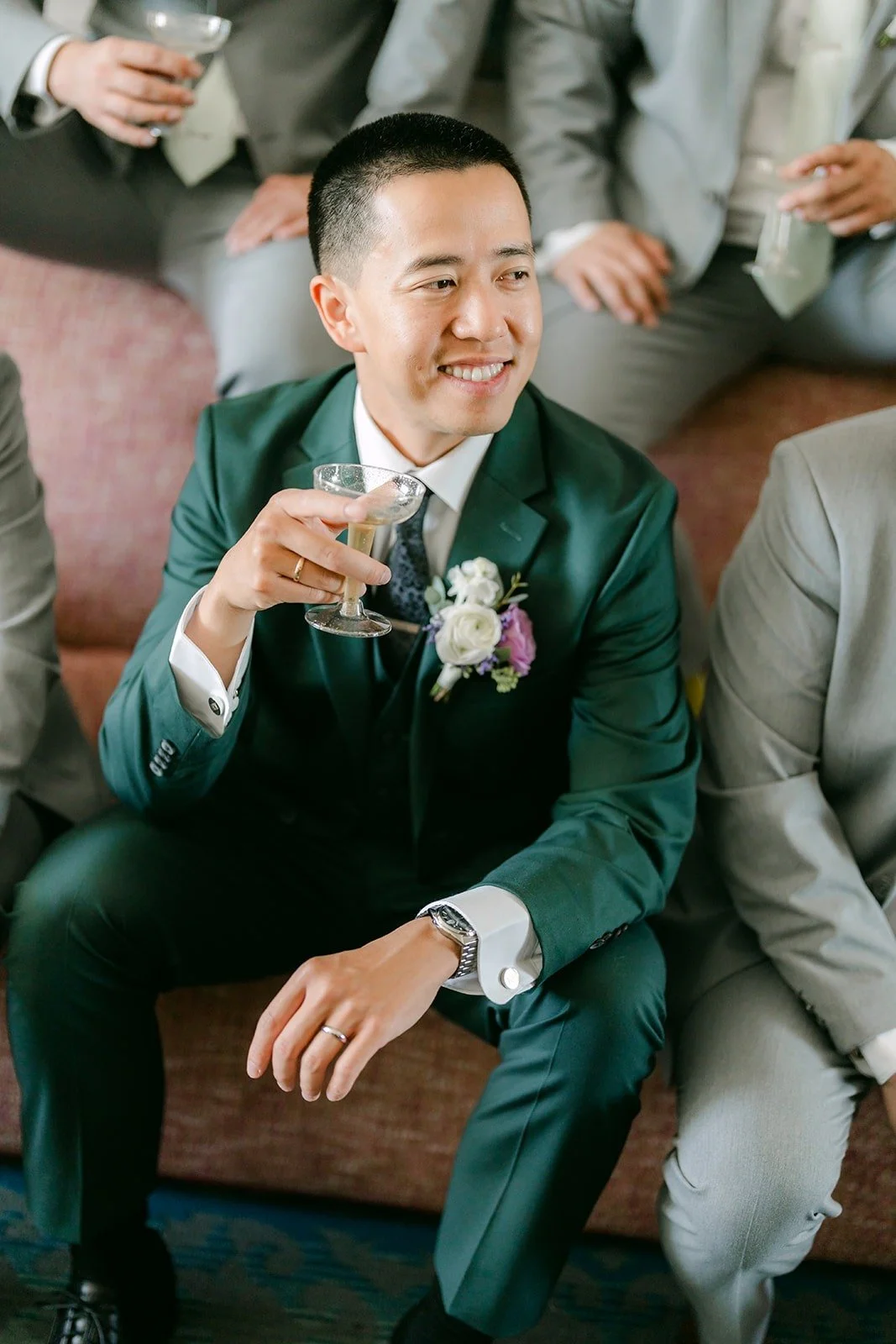 Kevin laughs with his groomsmen in his dark green suit, photographed by One and Only Production