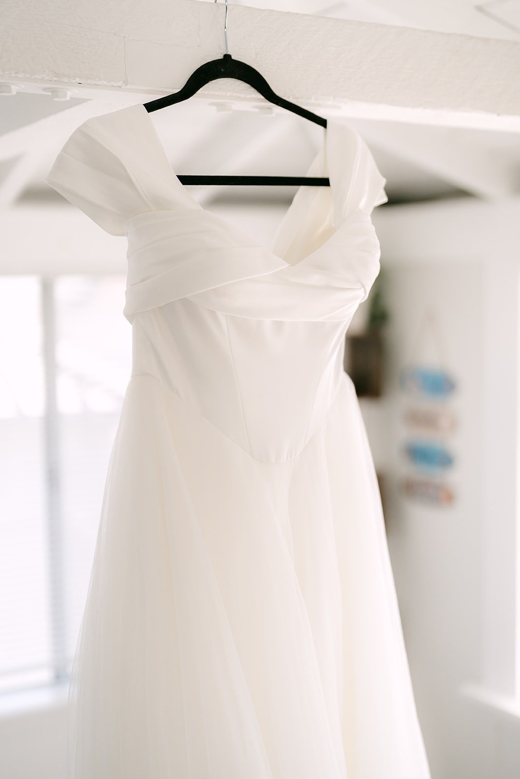 Jadee's wedding gown hanging in a bright white room in Newport Beach