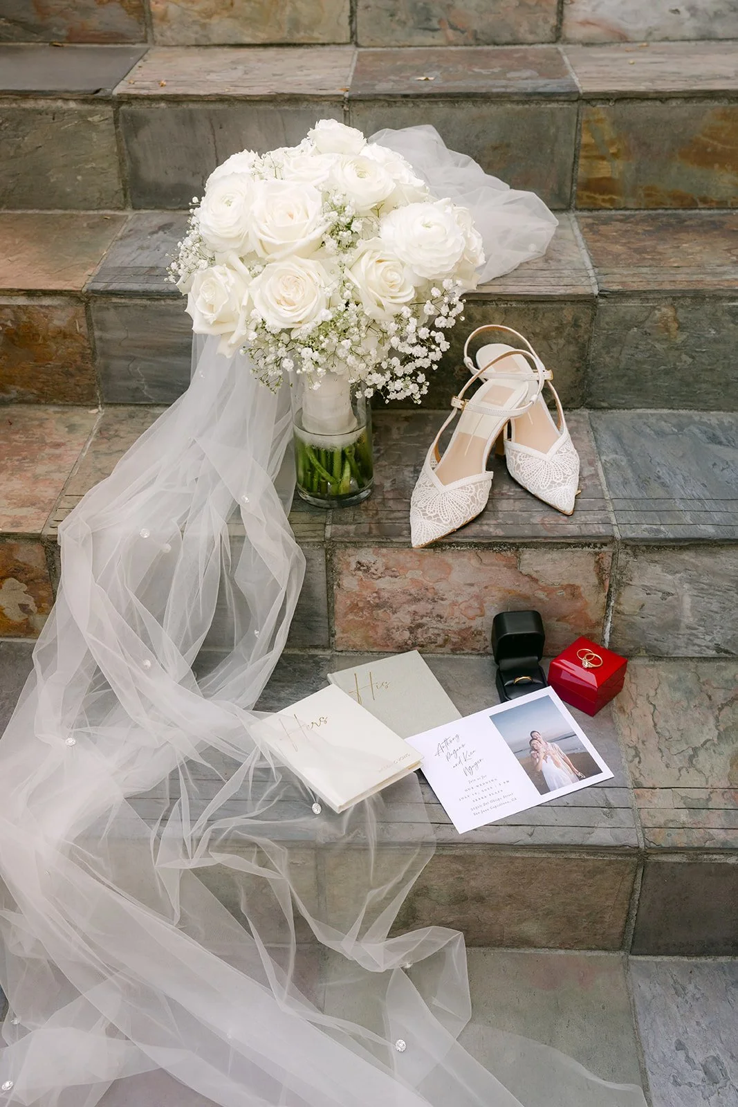 Bridal details with white bouquet, heels, veil and ring box on stone steps