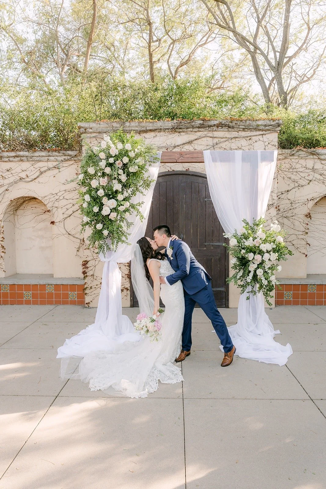 Alex dipping Kelli for a kiss in front of the floral arch at Los Robles Greens