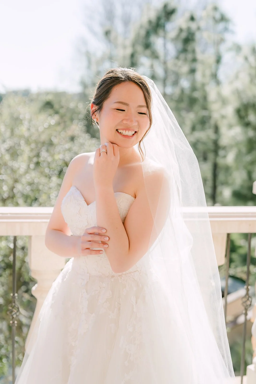 Bride smiling in her veil against the pine trees