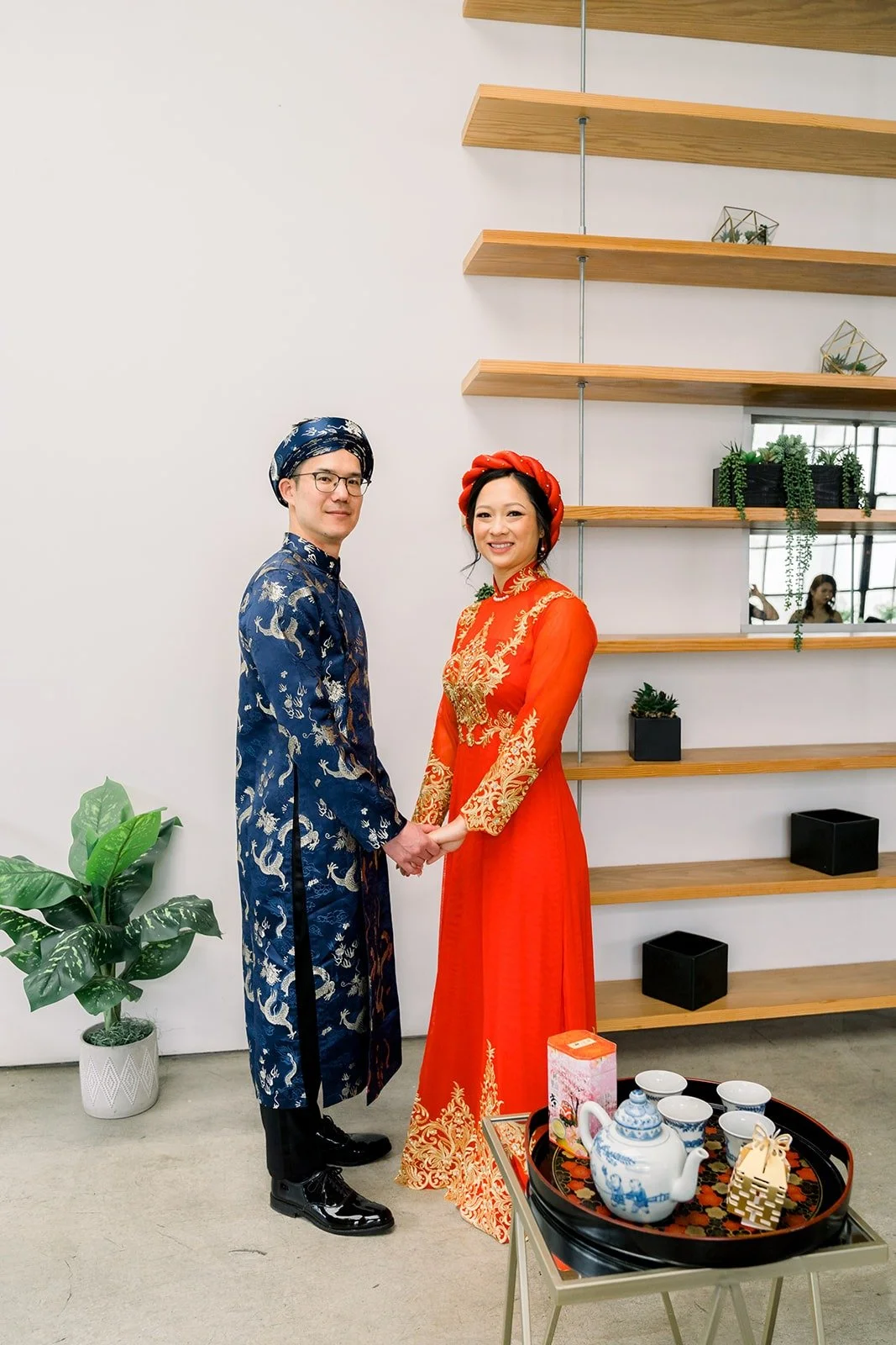Cindy and Alex in red and blue traditional attire beside the tea set