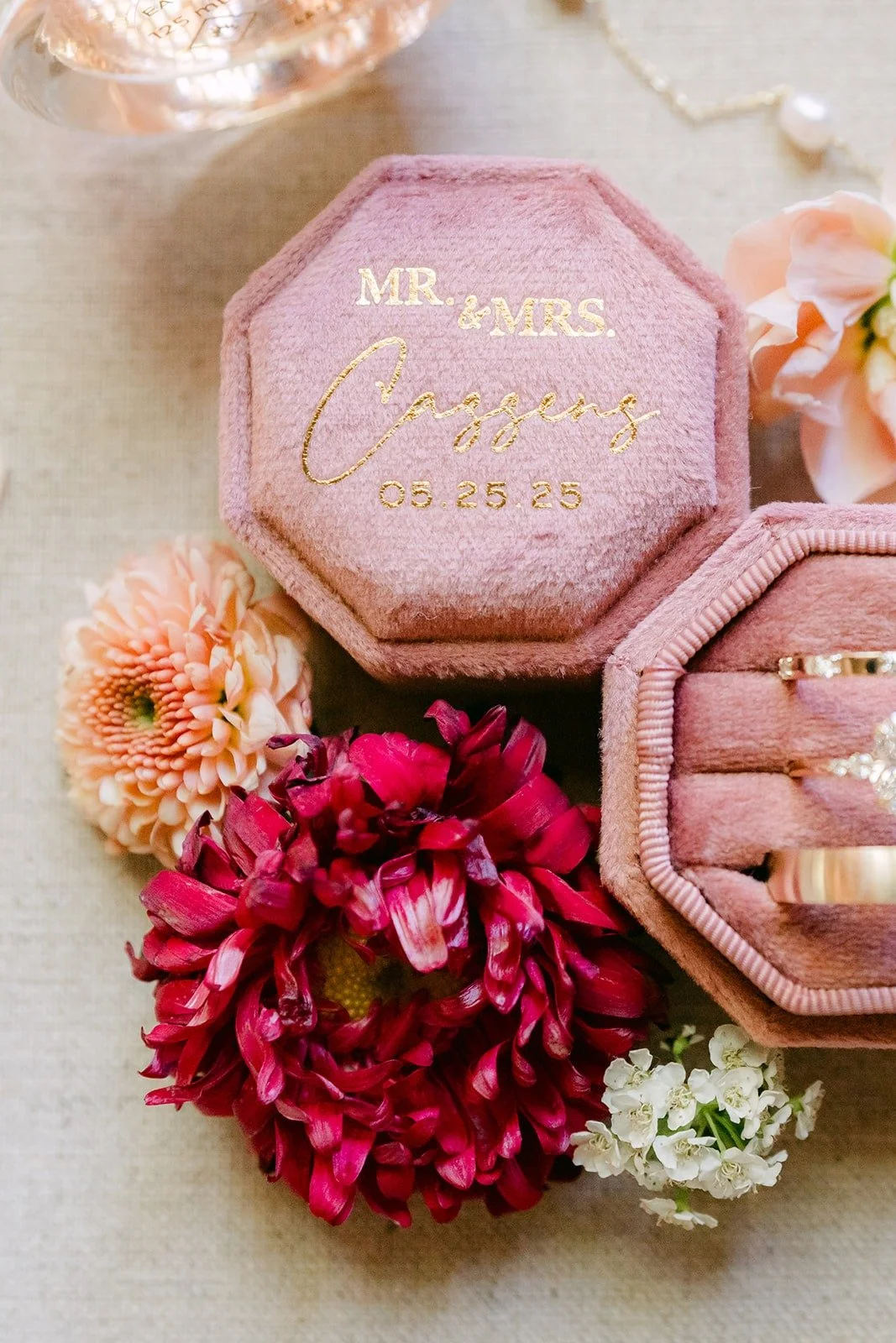 Two pink velvet ring boxes with the wedding rings, styled with red and blush flowers