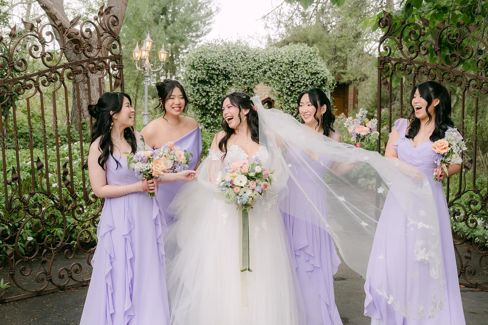Bridesmaids holding Kat's cathedral veil by the wrought iron gates