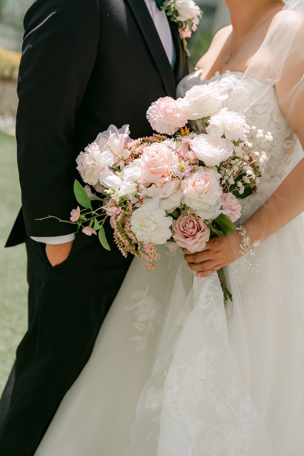 Close detail of Stella's blush and white bouquet held against James's tuxedo