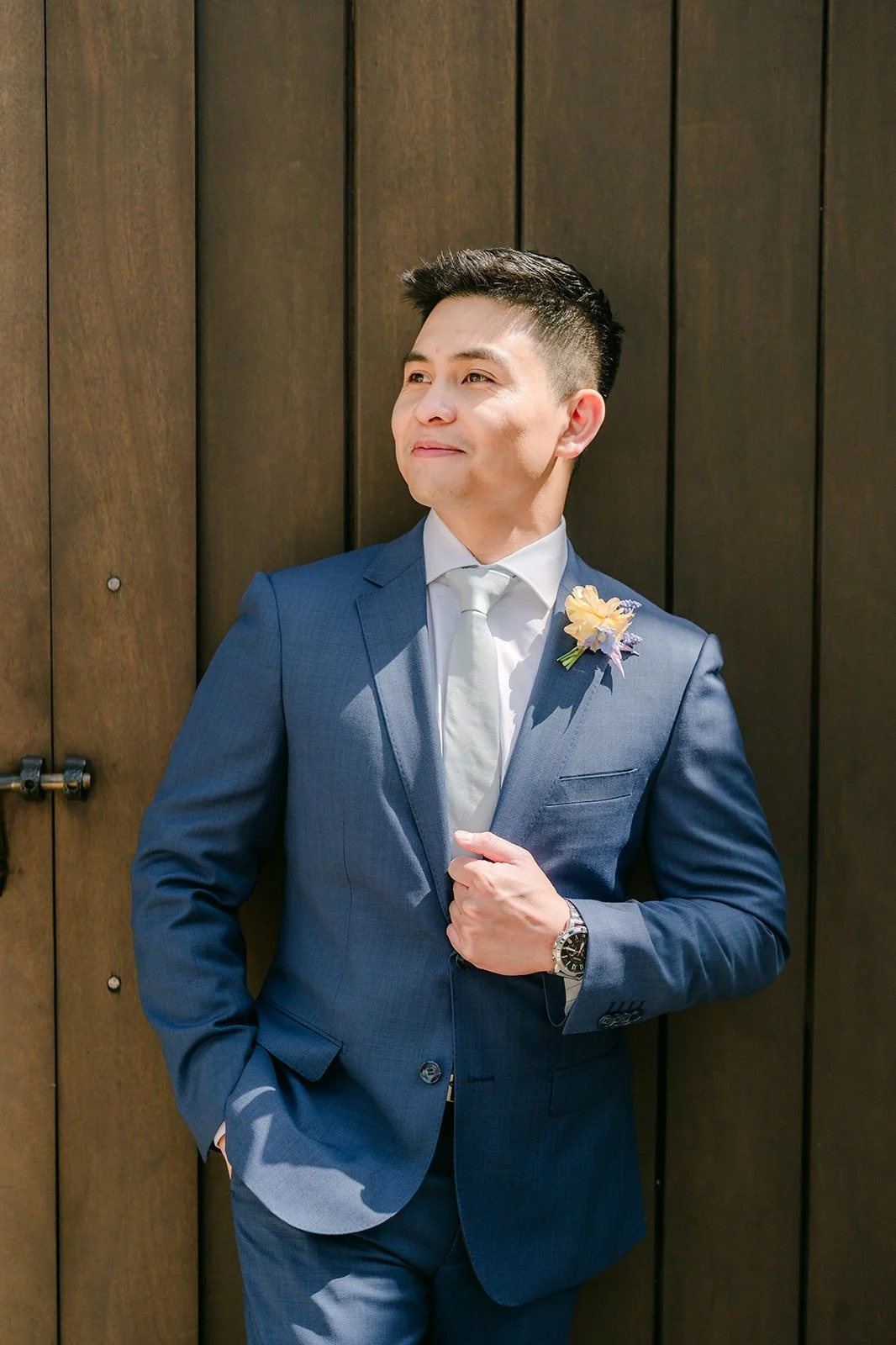 Jerrick leaning against a dark wood door in his blue suit and silver tie