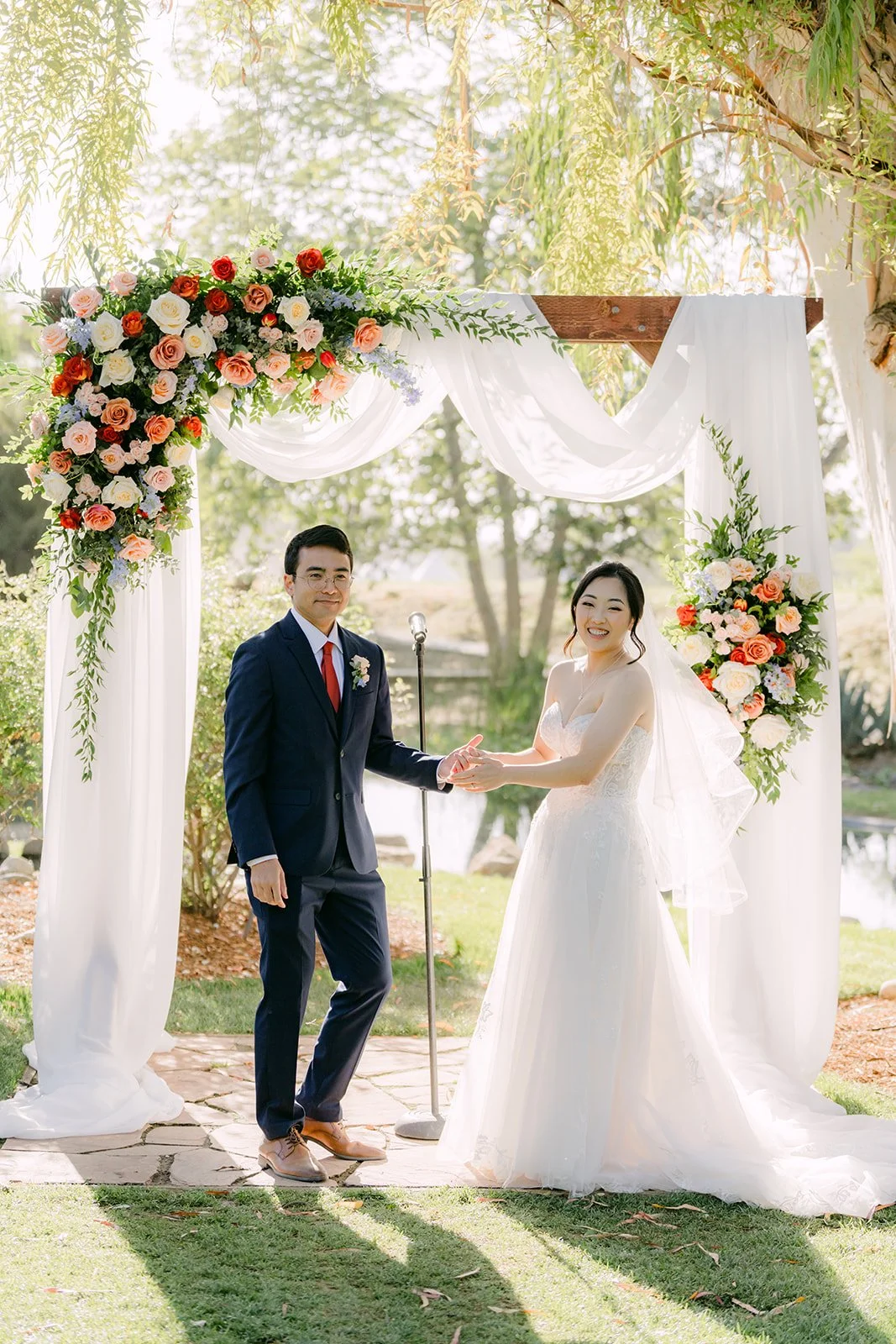 Yishan and Jonathan facing each other at the floral arch during the ceremony