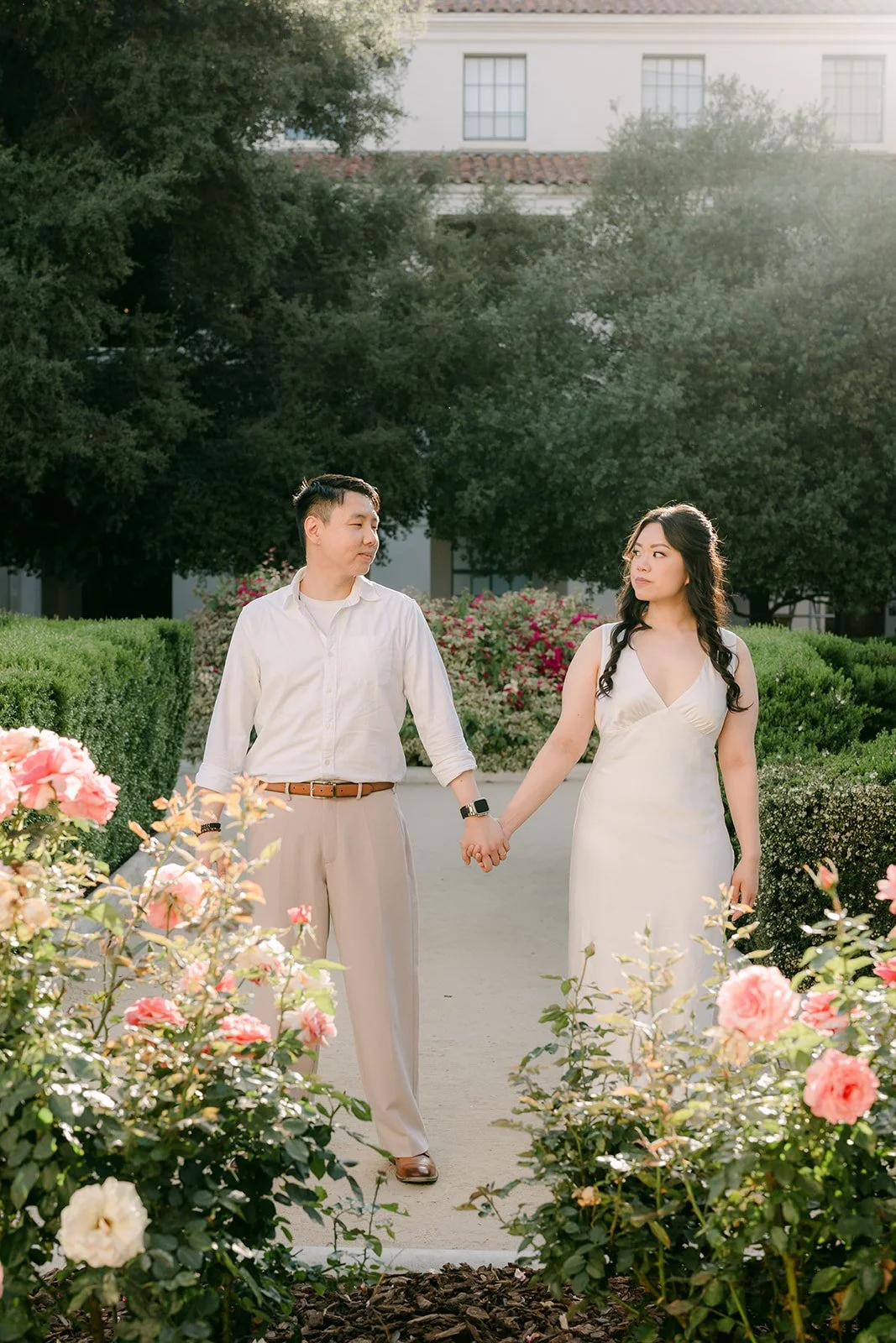 Emily and James walk hand in hand past blooming roses in the Pasadena City Hall garden.