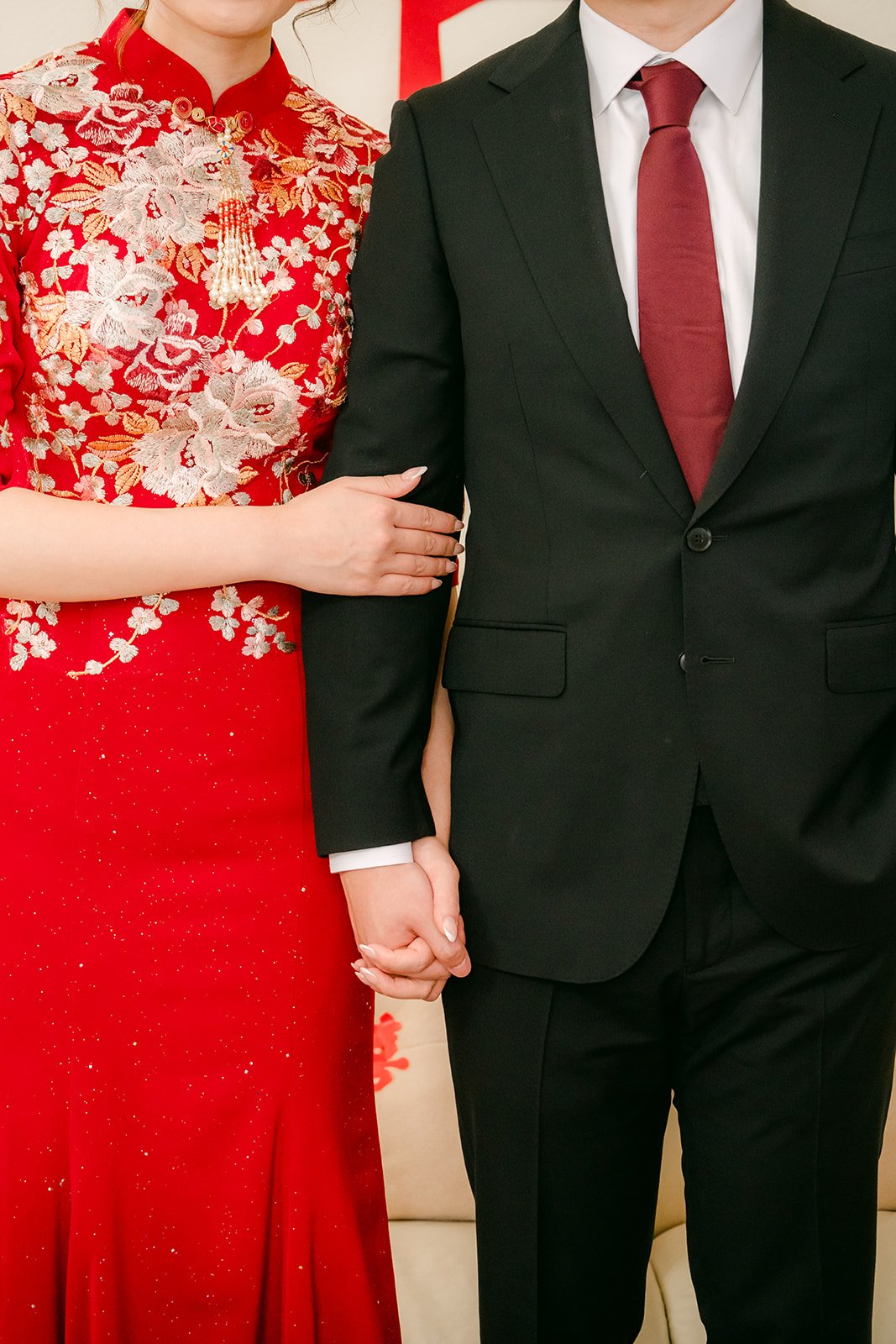 A bride in a red qipao holding the groom's arm, photographed by One and Only Production.
