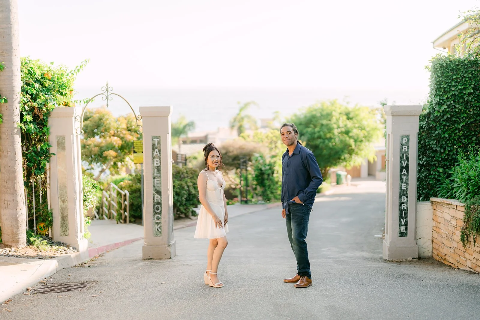 Amy and Michael standing at a gated garden drive with the ocean in the distance.