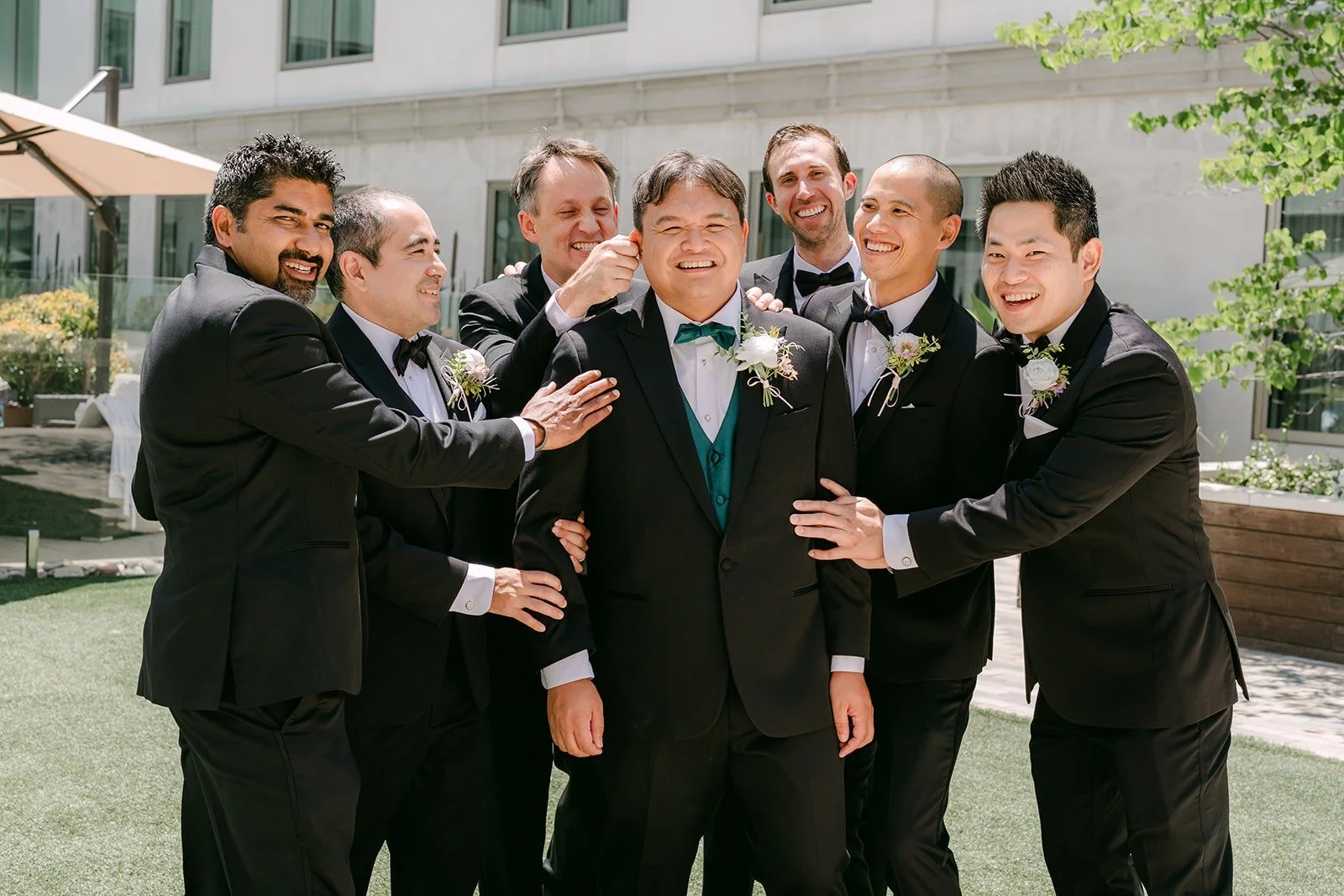 The groomsmen crowding around James with big smiles on the lawn, photographed by One and Only Production