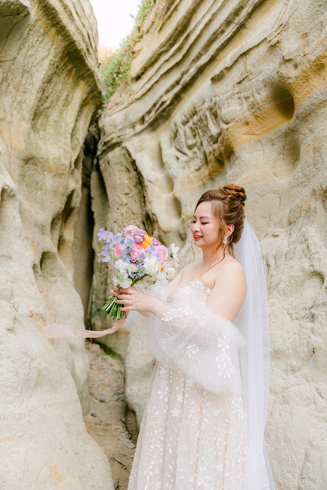 Joanna holding her bouquet against the sculpted sandstone, her veil trailing