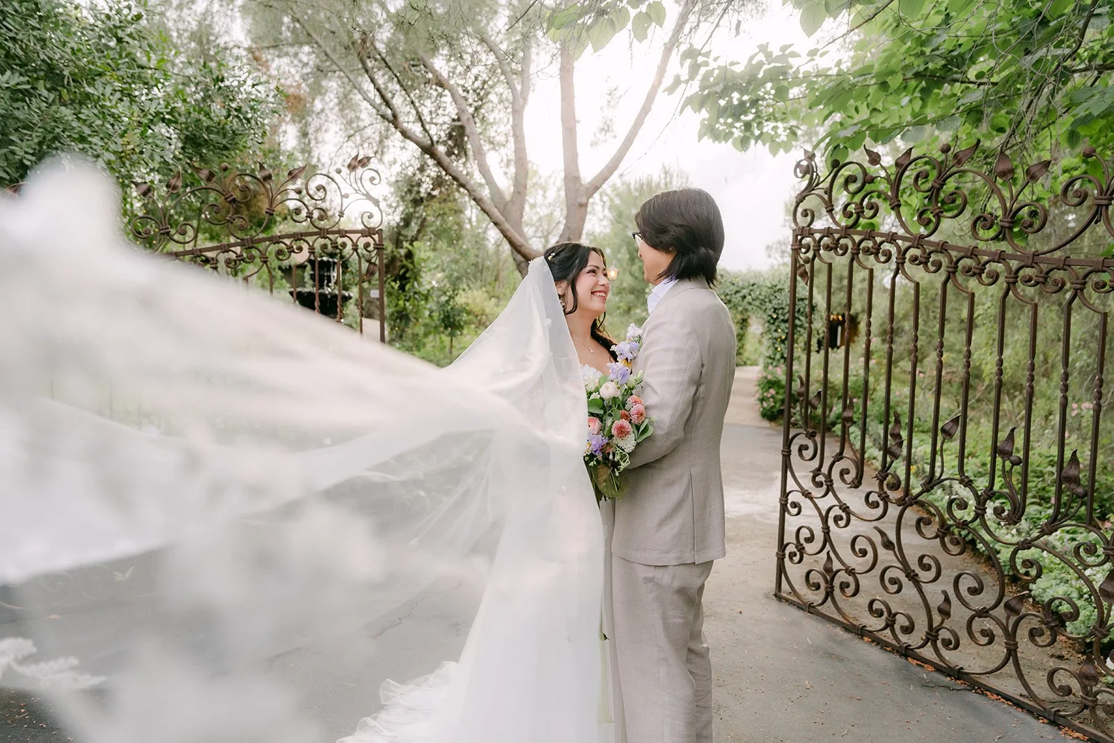 Veil billowing in the breeze as Kat and Mike stand by the iron gates