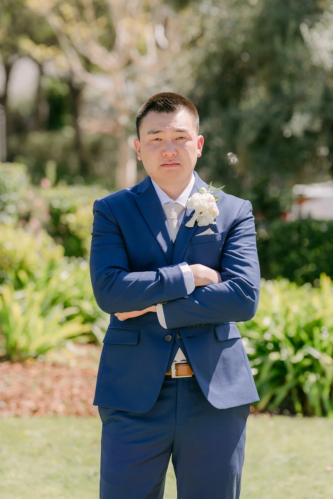 Alex in his navy suit with arms crossed in the garden at Los Robles Greens