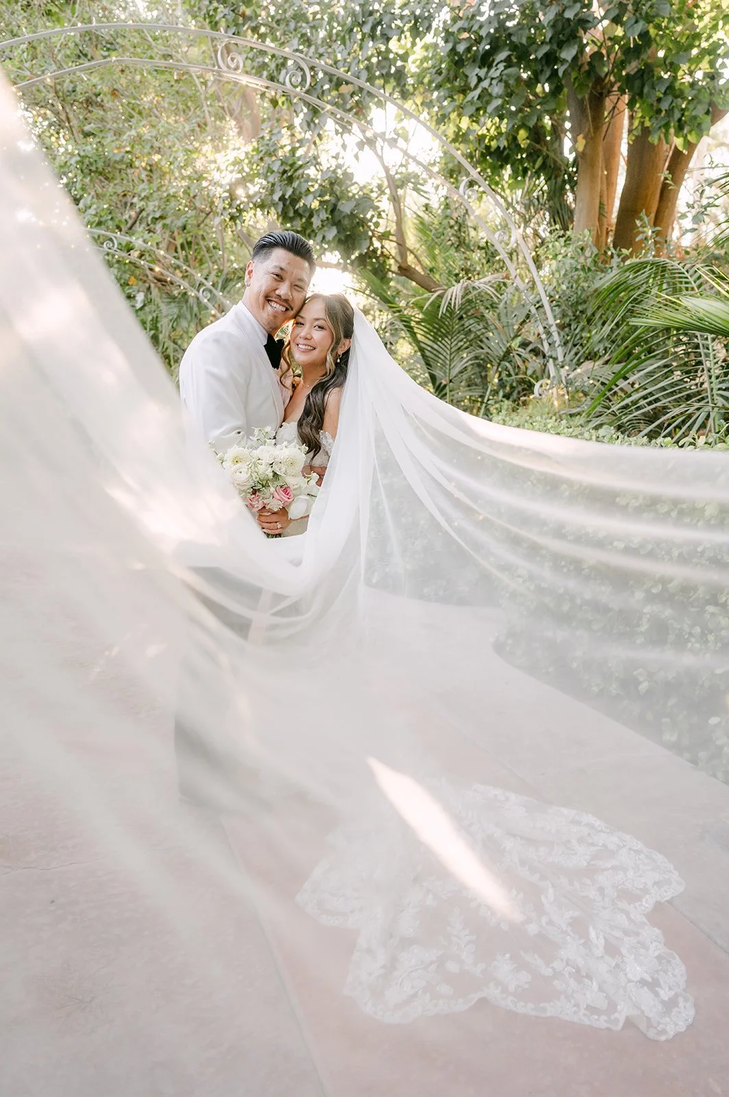 Caryl and Nicole kissing with her veil flowing behind them at Eden Gardens.