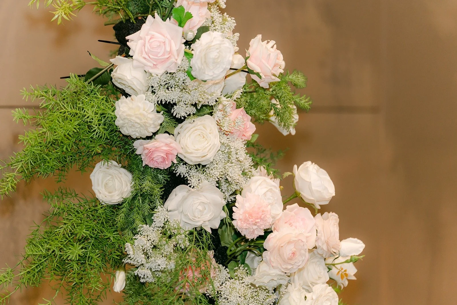 Blush and white roses arranged with greenery on the ceremony arch