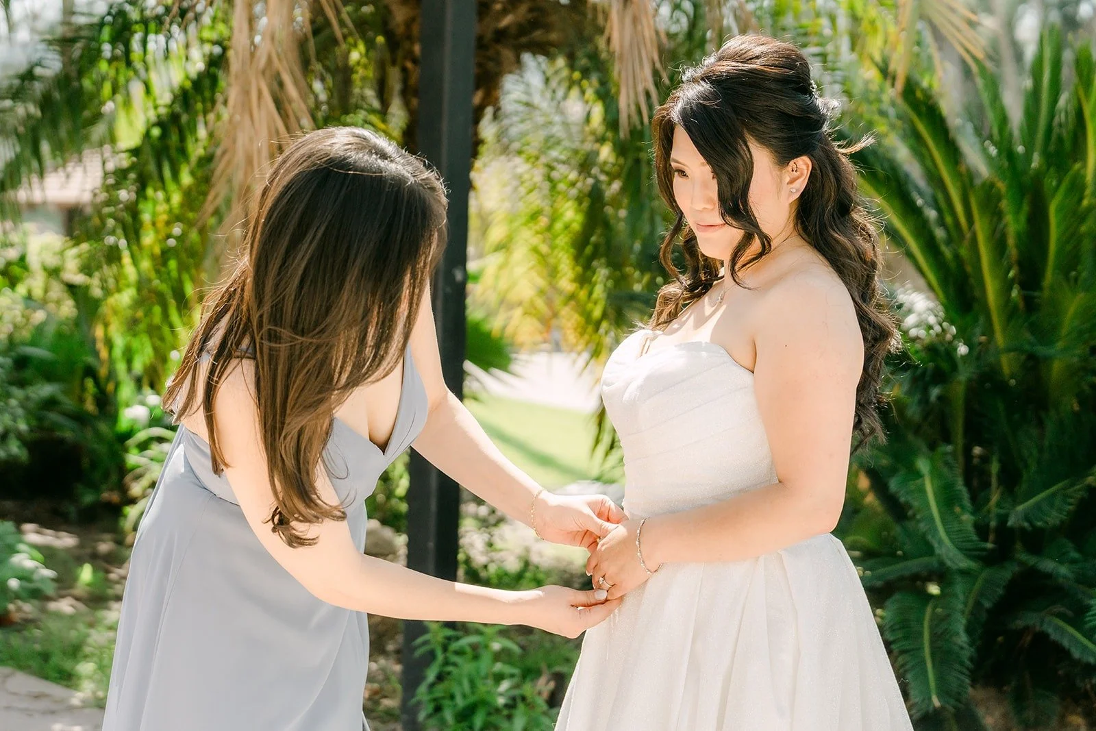 A bridesmaid in dusty blue helping Florence with her gown