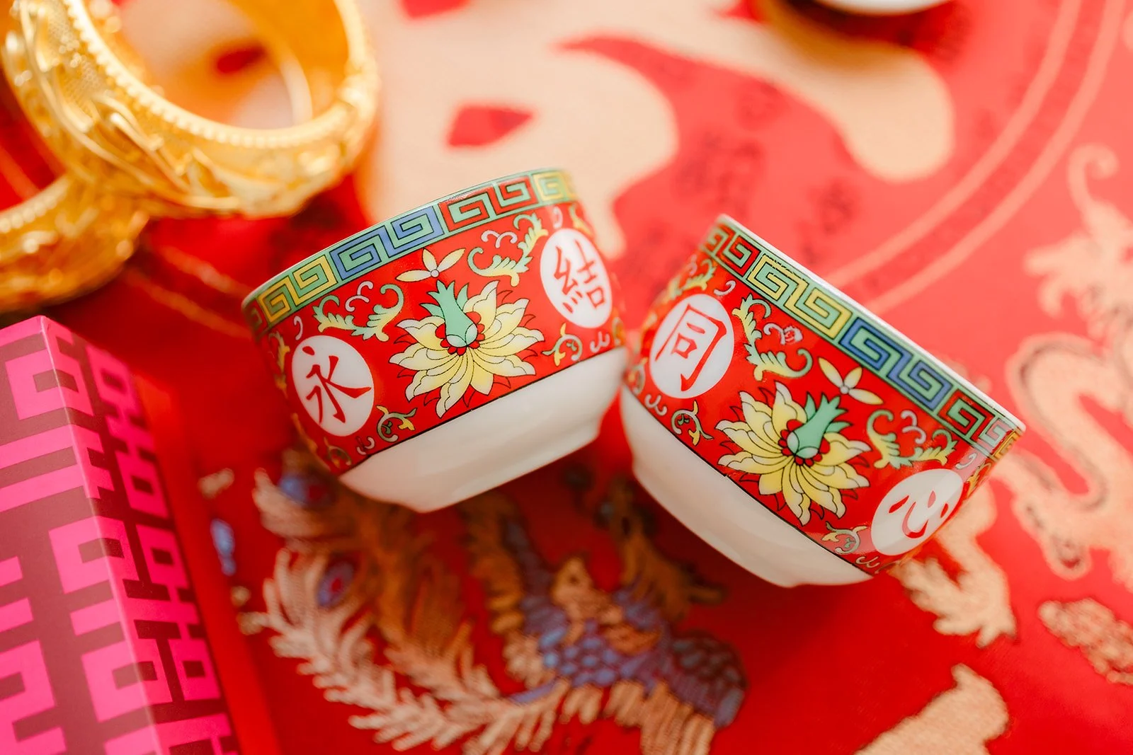 Red and white double happiness teacups beside gold bangles.