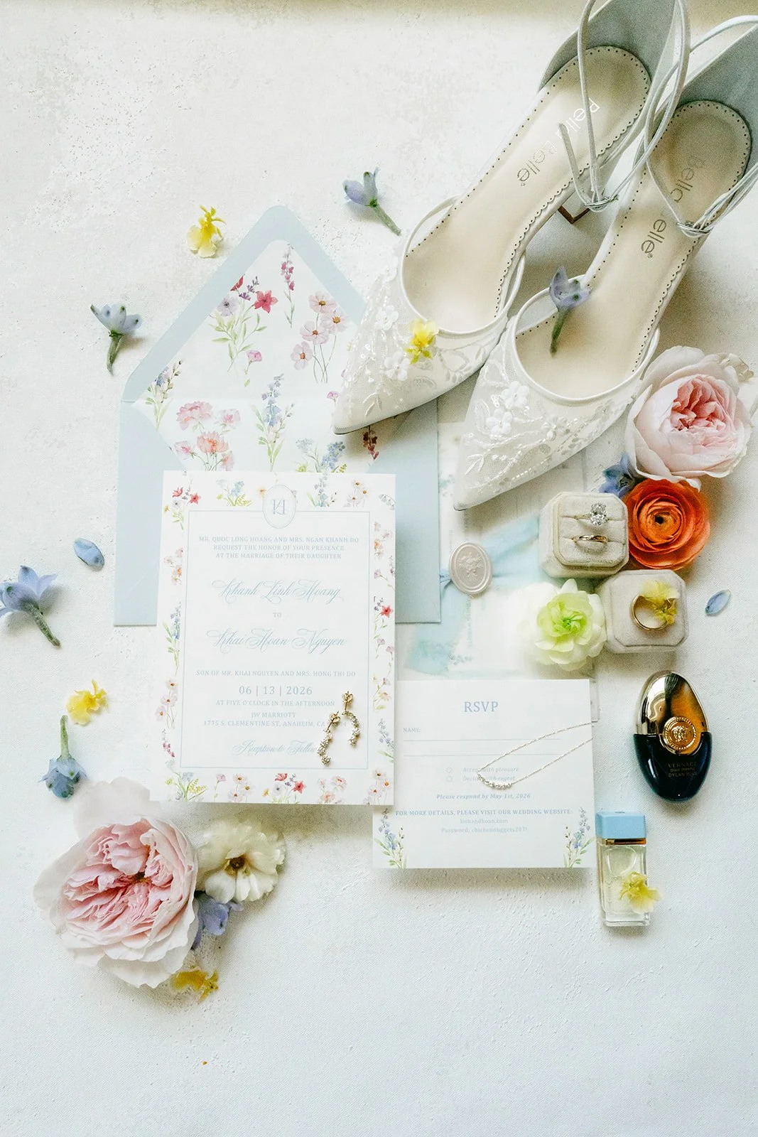 Flat lay of Linh's lace heels, watercolor floral invitation suite and pastel blooms on a light blue backdrop