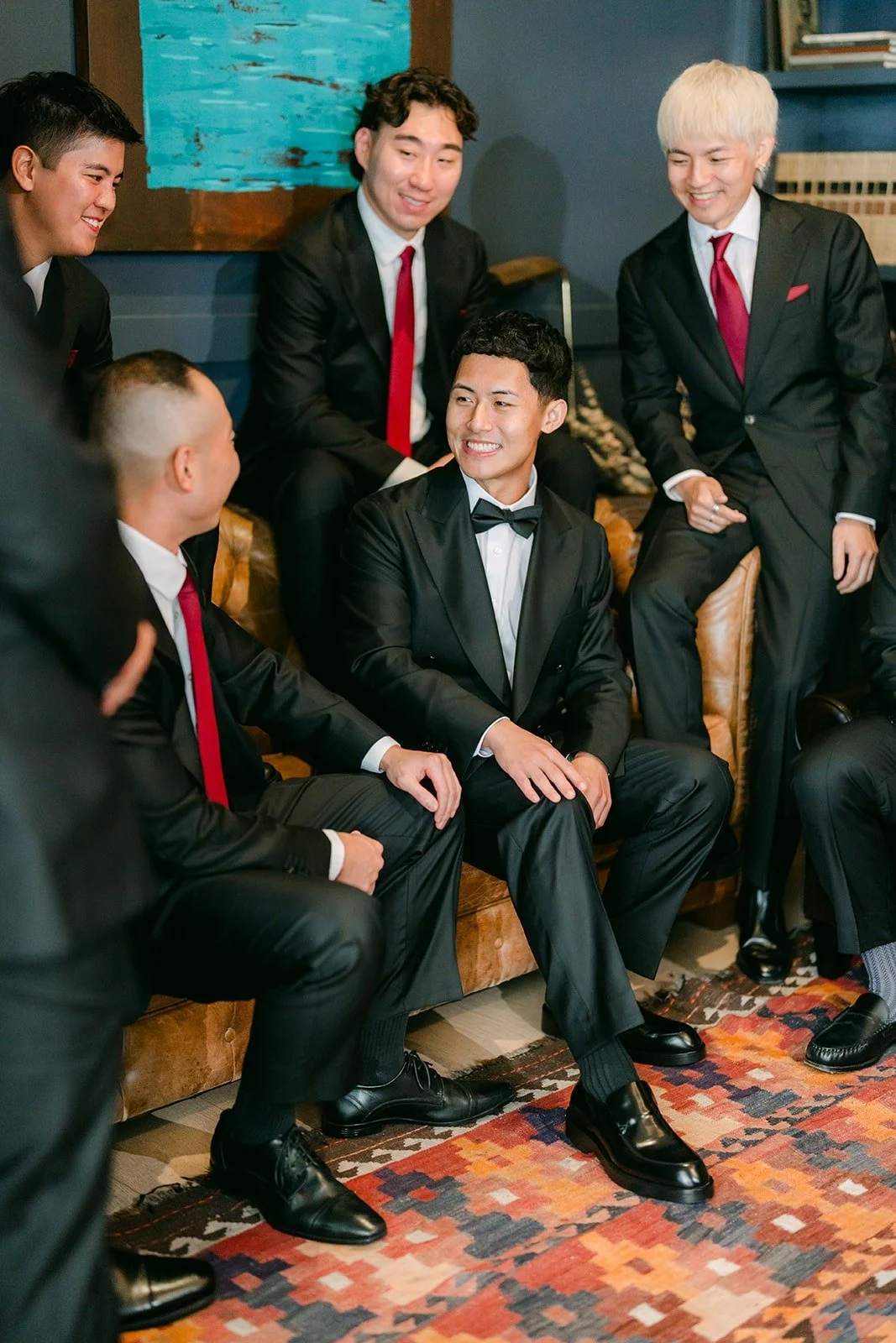 Richard and his groomsmen in black tuxedos and red ties laughing together