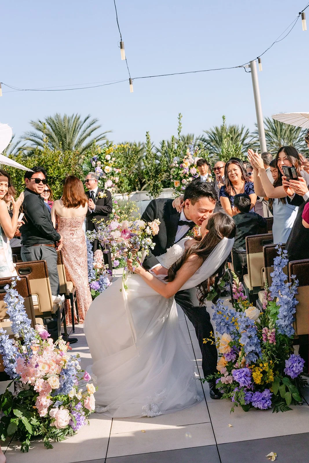 Recessional dip kiss surrounded by guests and pastel aisle florals