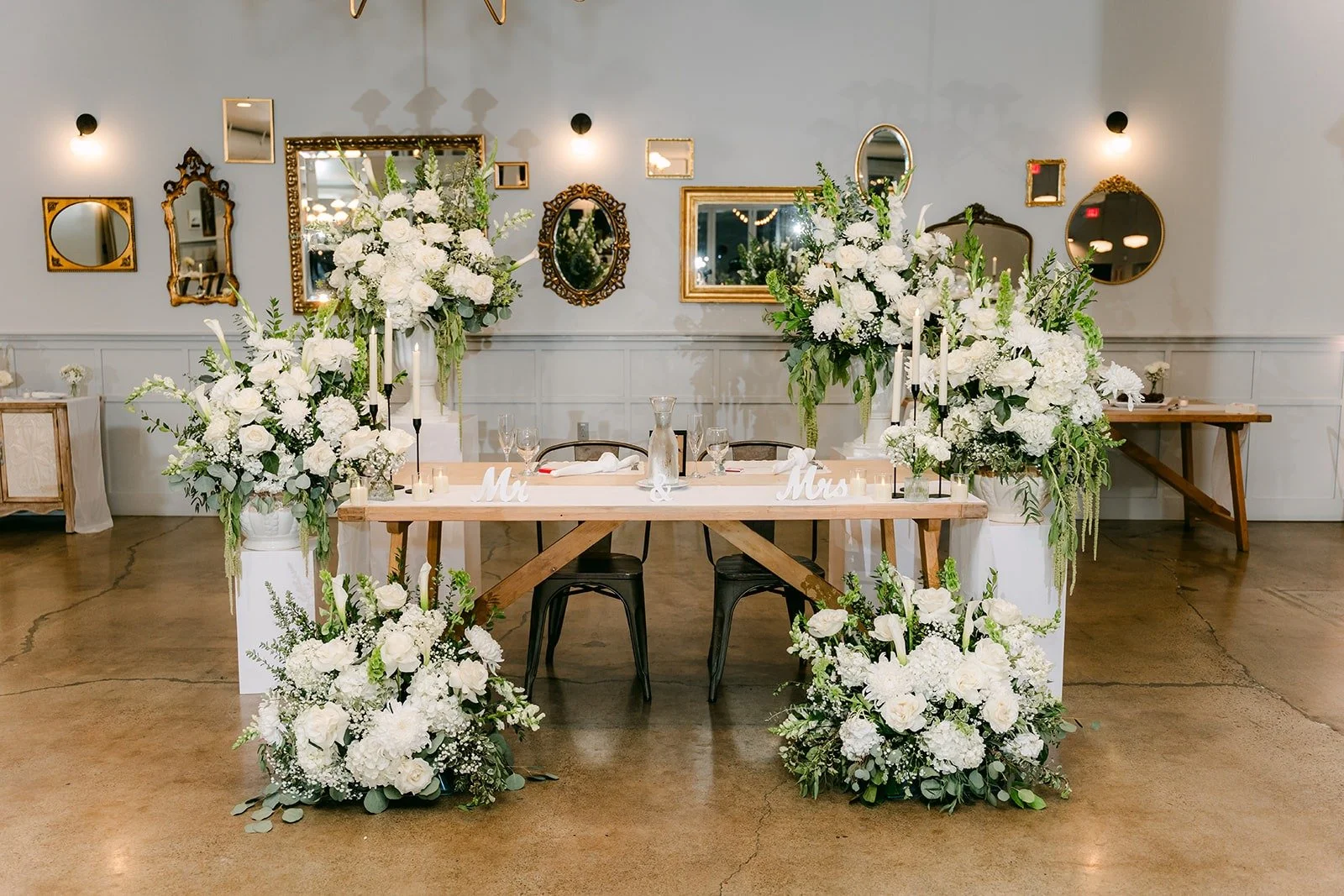 The sweetheart table banked in white flowers under gold framed mirrors