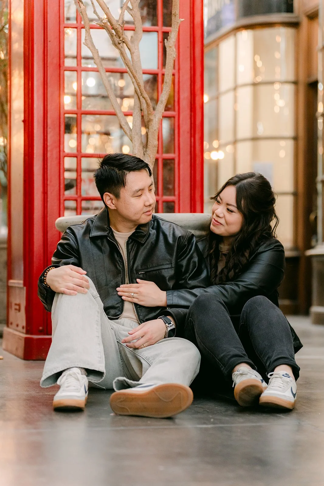 Emily and James sit on the floor beside the red phone booth.