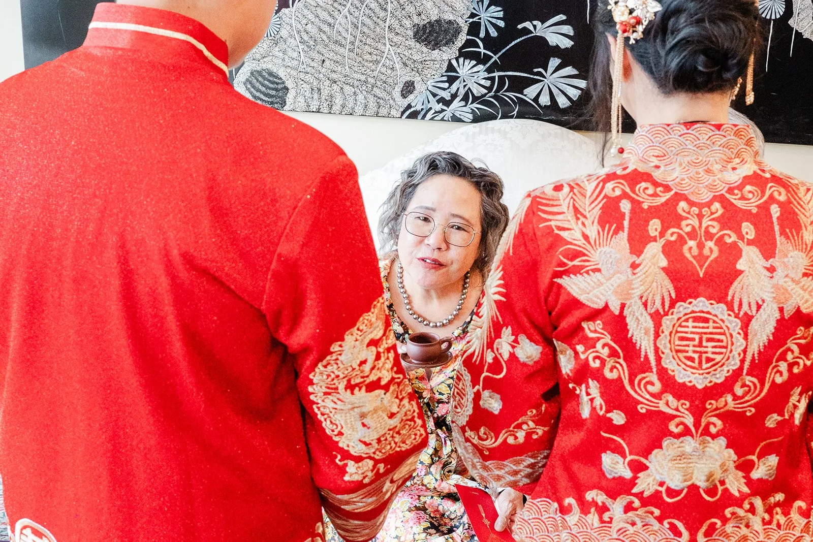 A bride and groom in red serving tea to their grandmother during the tea ceremony.