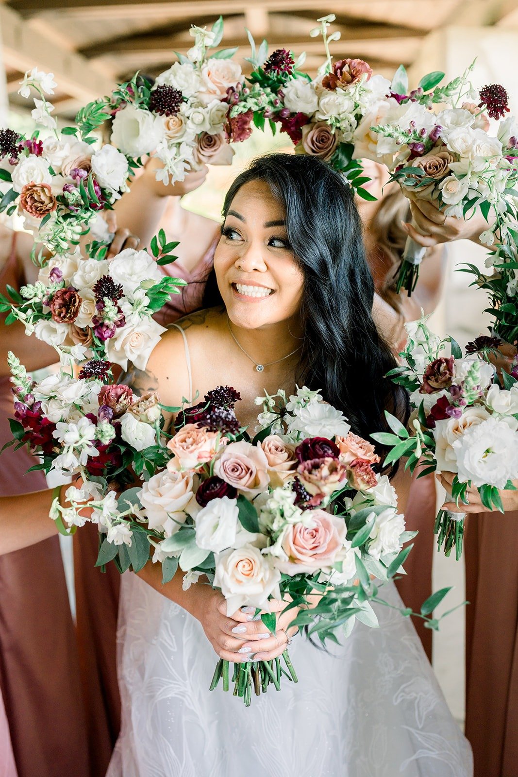 Betsy holds her bouquet inside a ring of burgundy and blush flowers, photographed by One and Only Production
