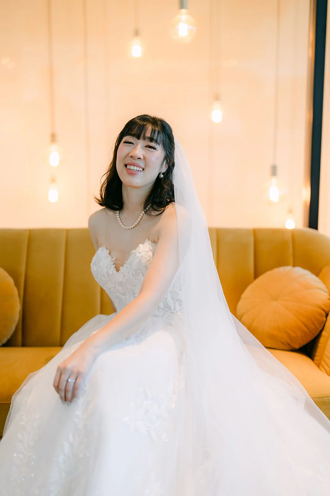Bridal portrait of Vivian laughing on the mustard sofa at The Colony House