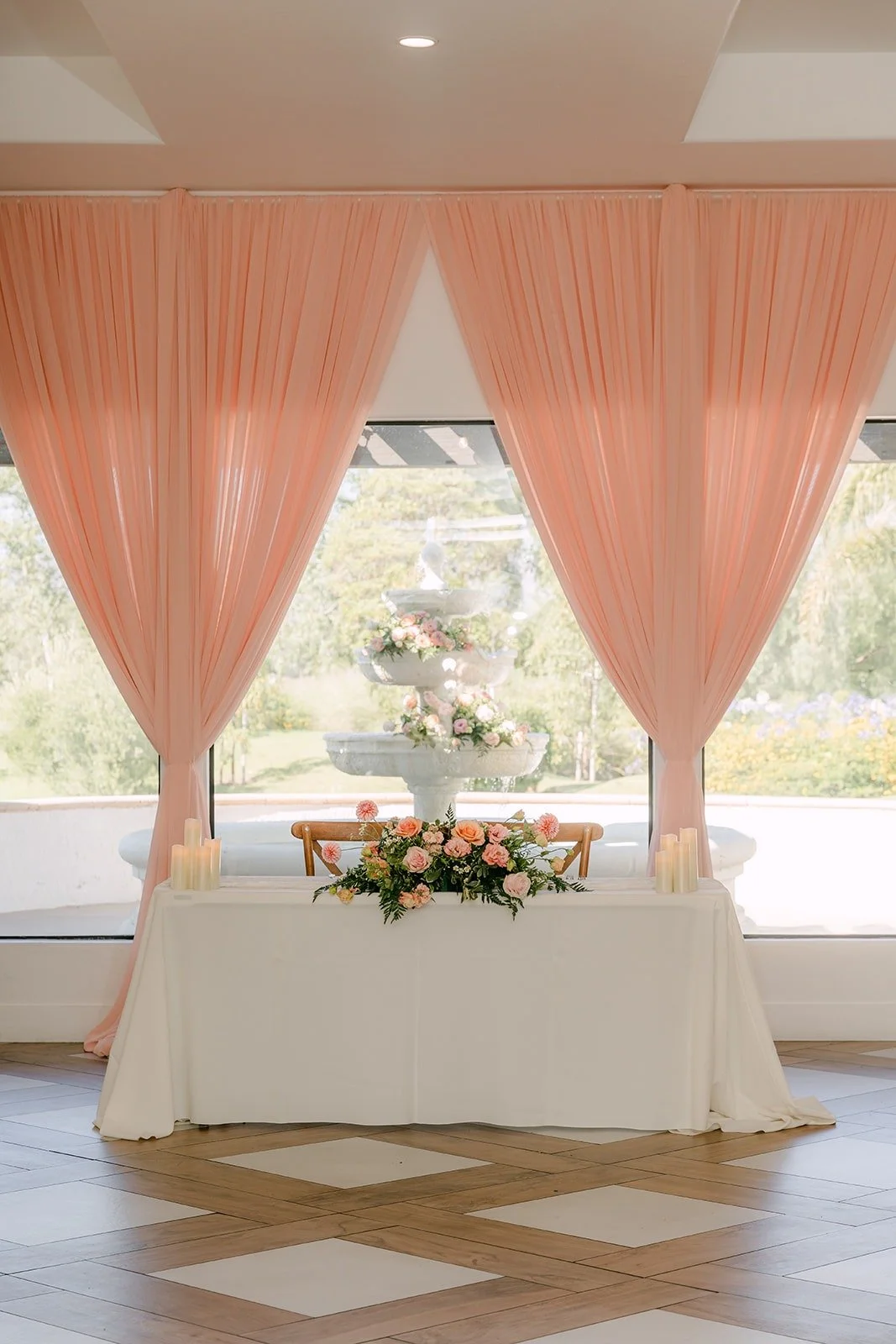 The sweetheart table set against blush pink drapes and a wall of windows