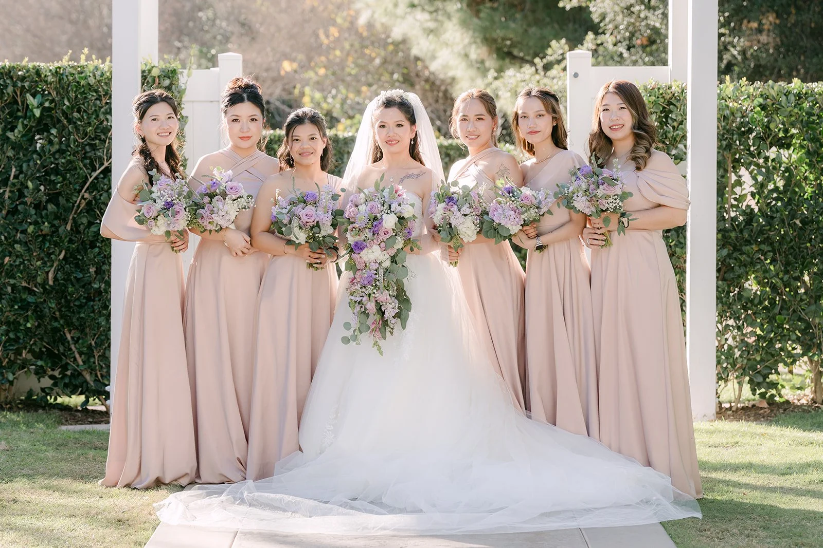Kate with her bridesmaids in blush dresses under the white pergola.