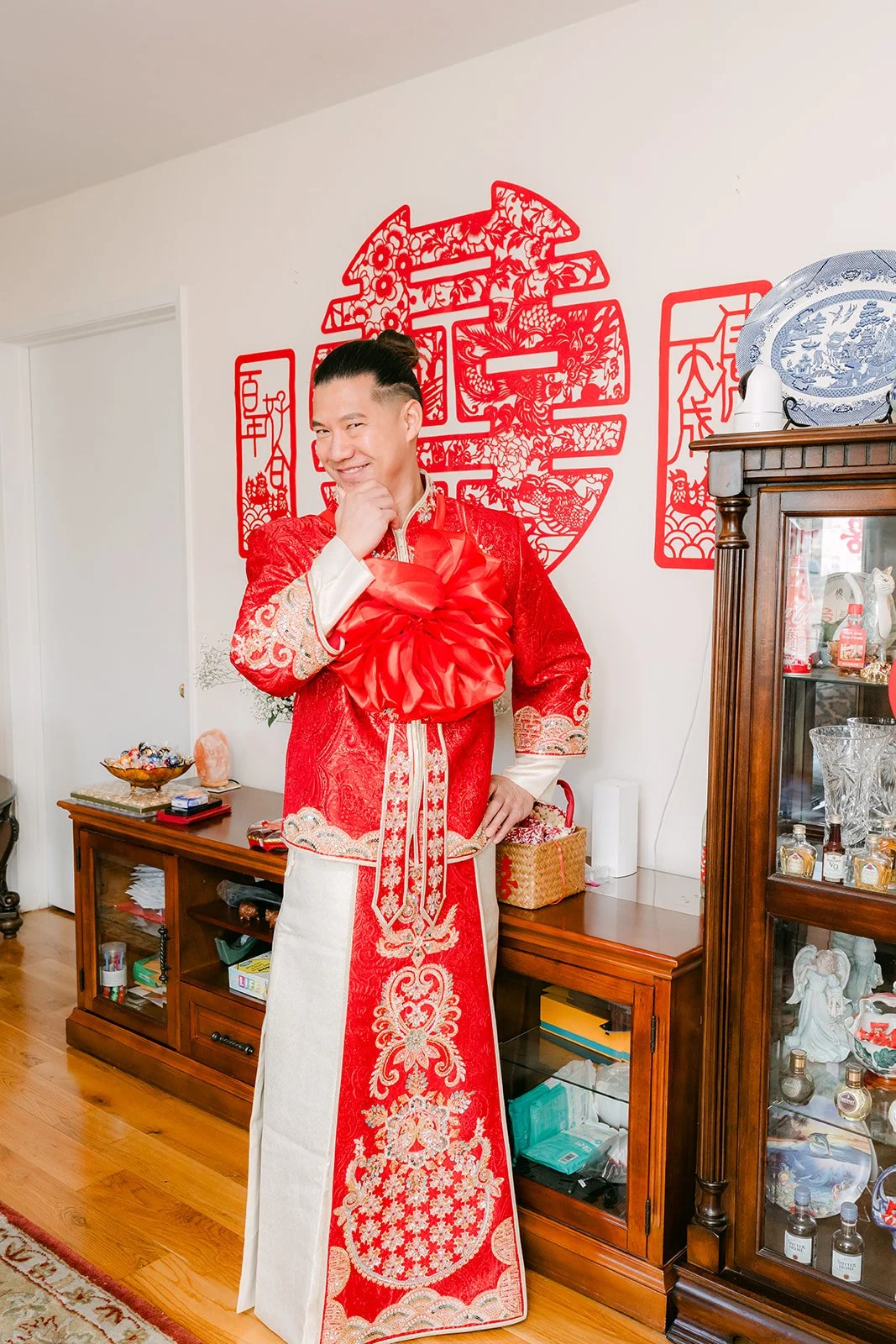 A groom in a red and white changshan in the family living room.