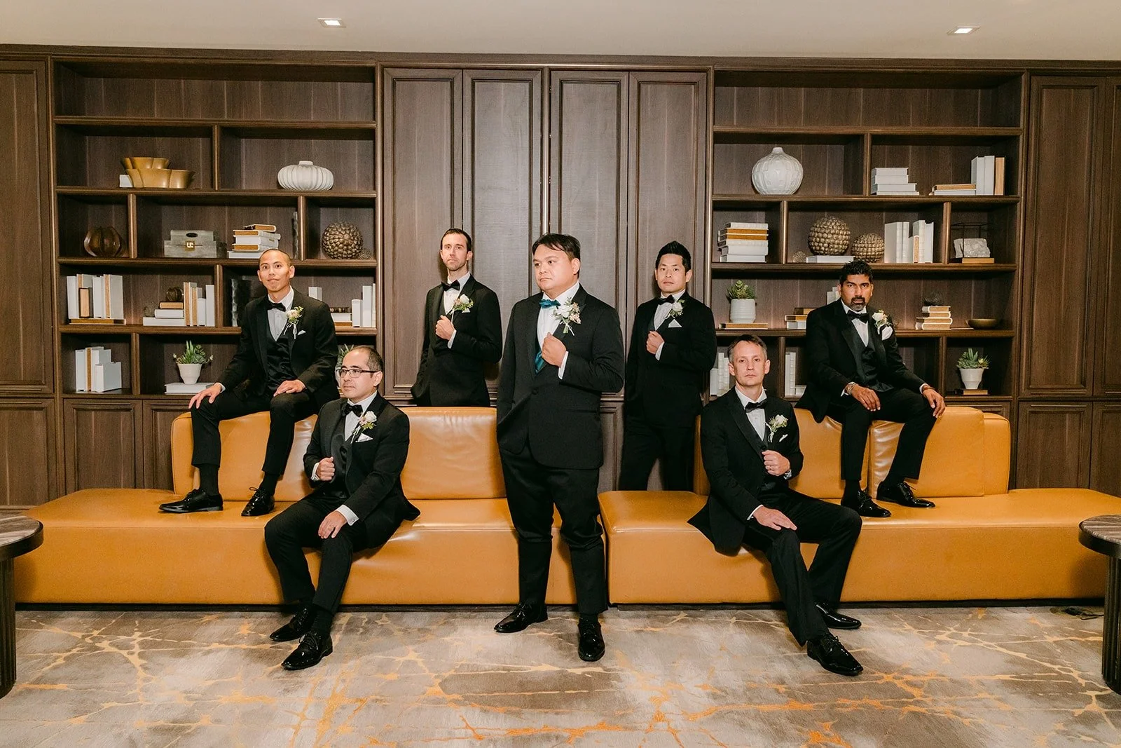 James and his groomsmen posed on the orange sofa in front of tall wooden bookshelves