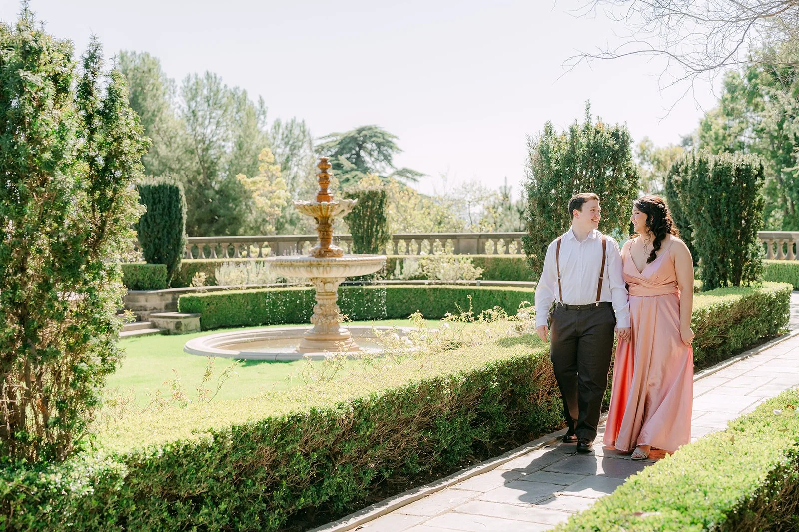 The couple walking past the fountain along the formal garden path.