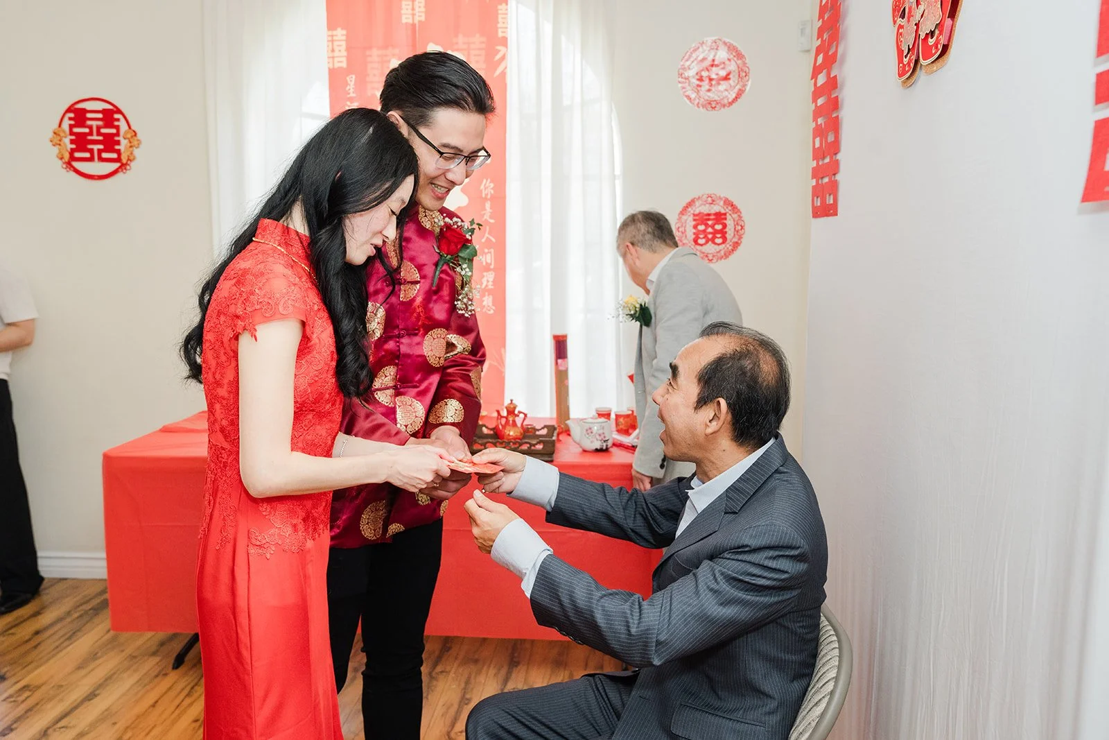 The couple offering tea to a seated relative.