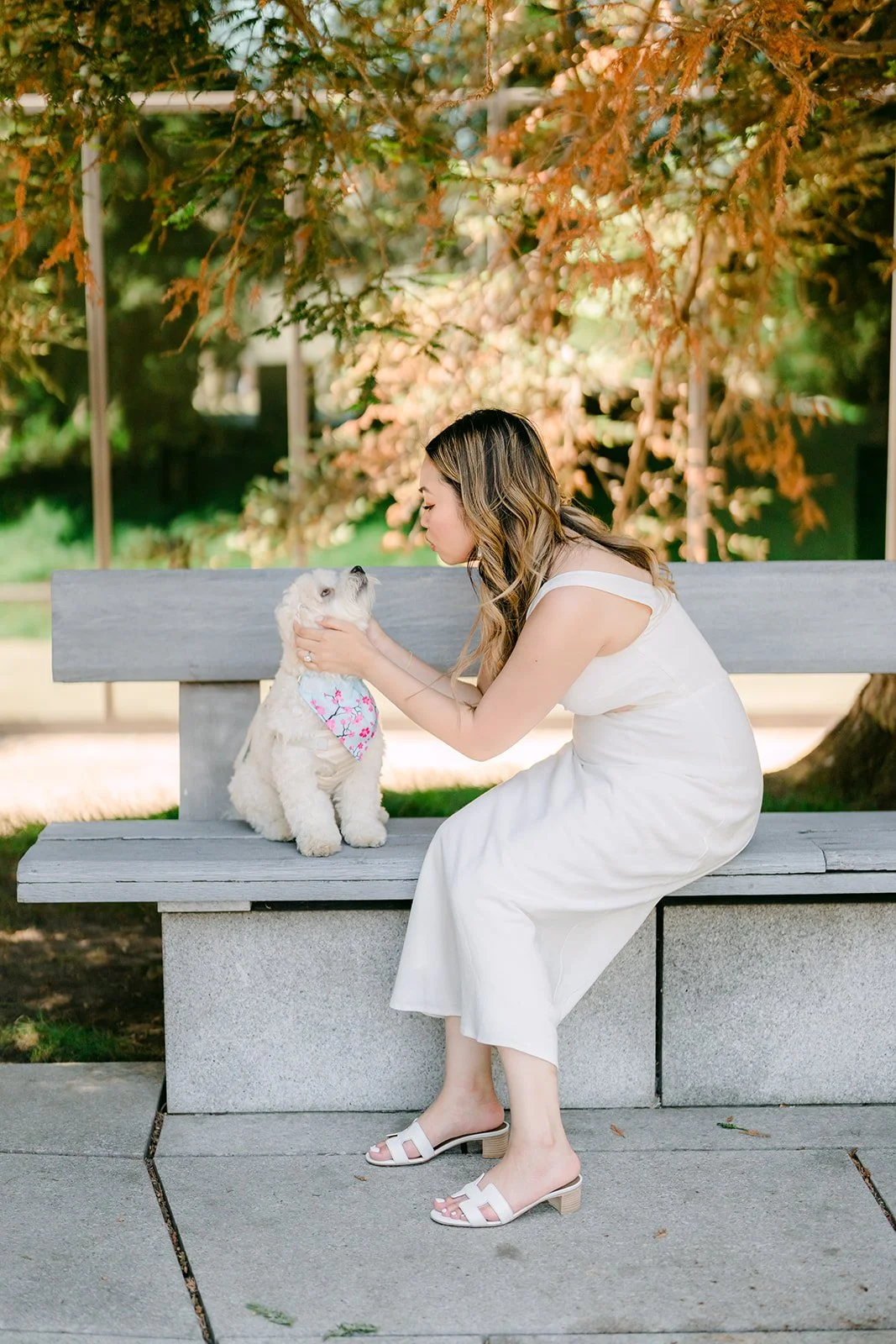 Stephanie kneels on a stone bench to greet Tofu beneath the trees.