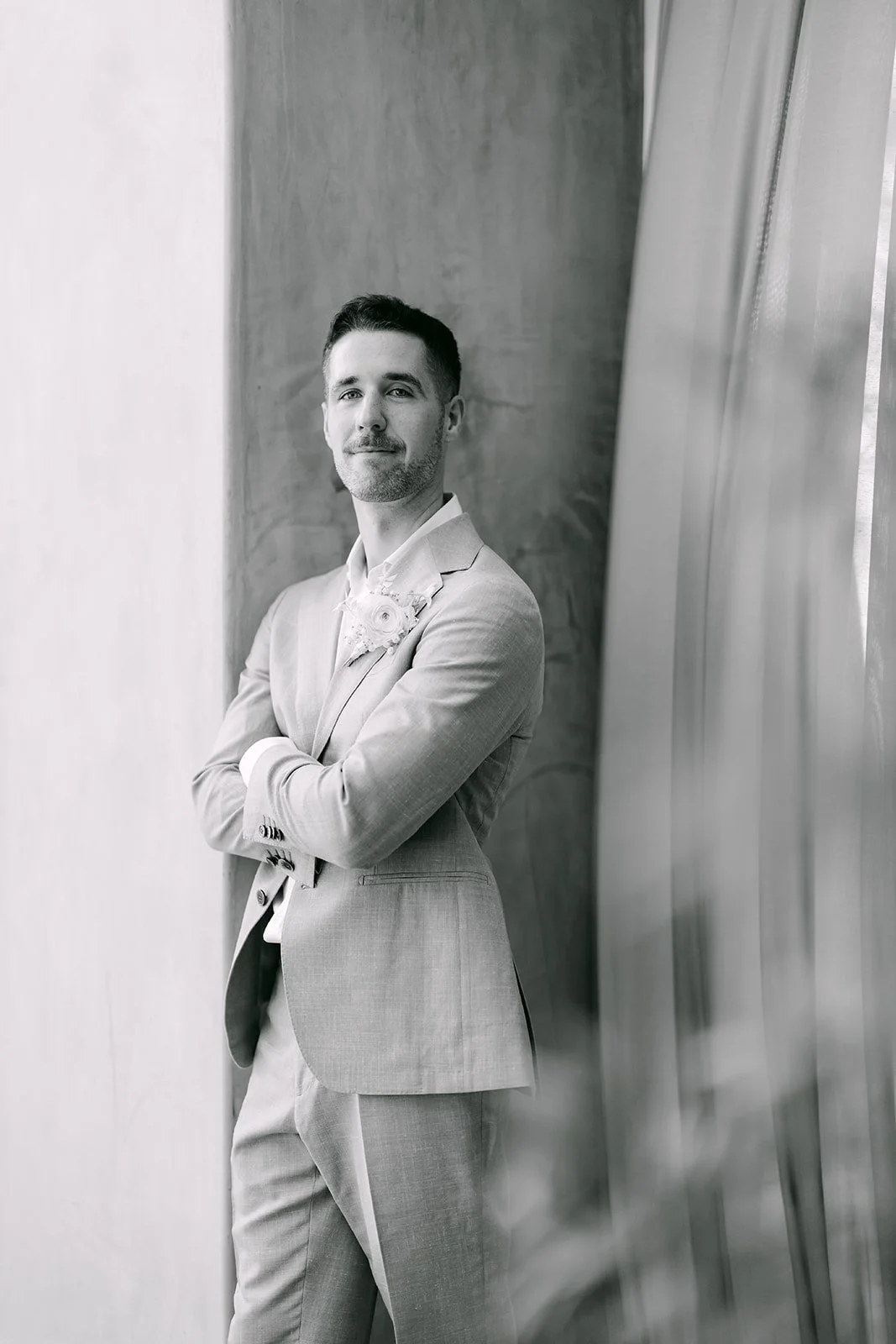 Black and white portrait of the groom leaning against the wall with arms crossed