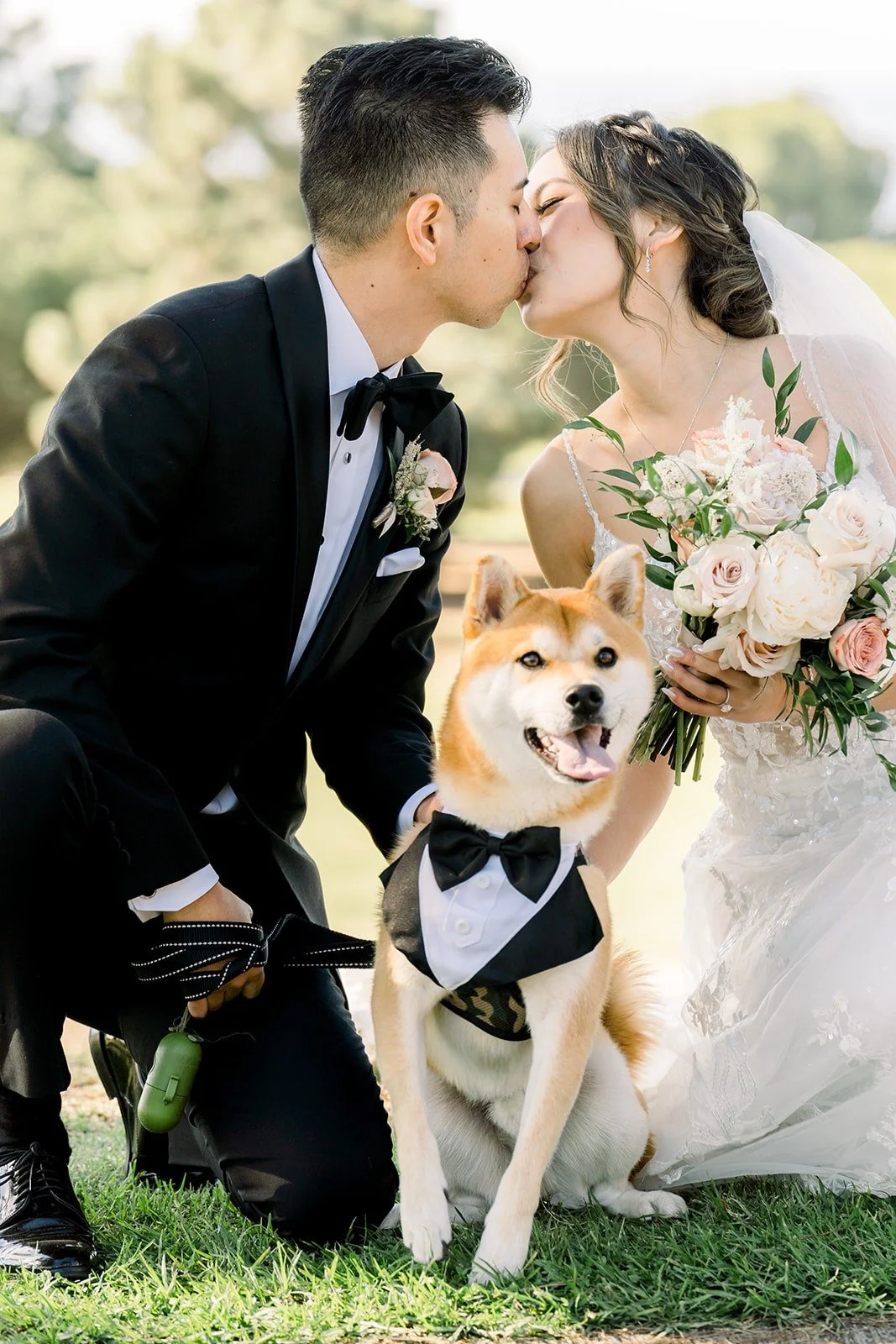 Josephine and David kissing with their dog in a bow tie between them