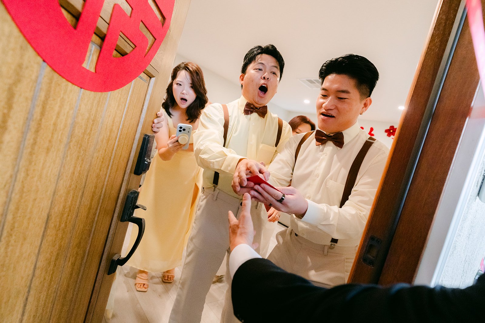 The groom and groomsmen pushing red envelopes through the door to the bridesmaids.