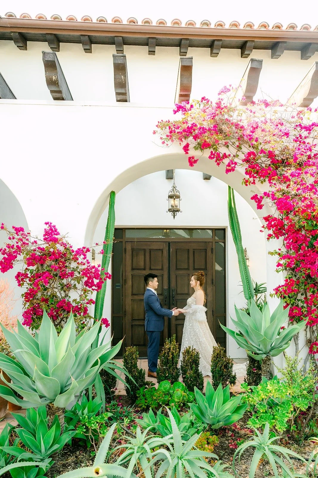 Joanna and Jerrick by the arched doorway in the La Ventura courtyard, framed by bougainvillea