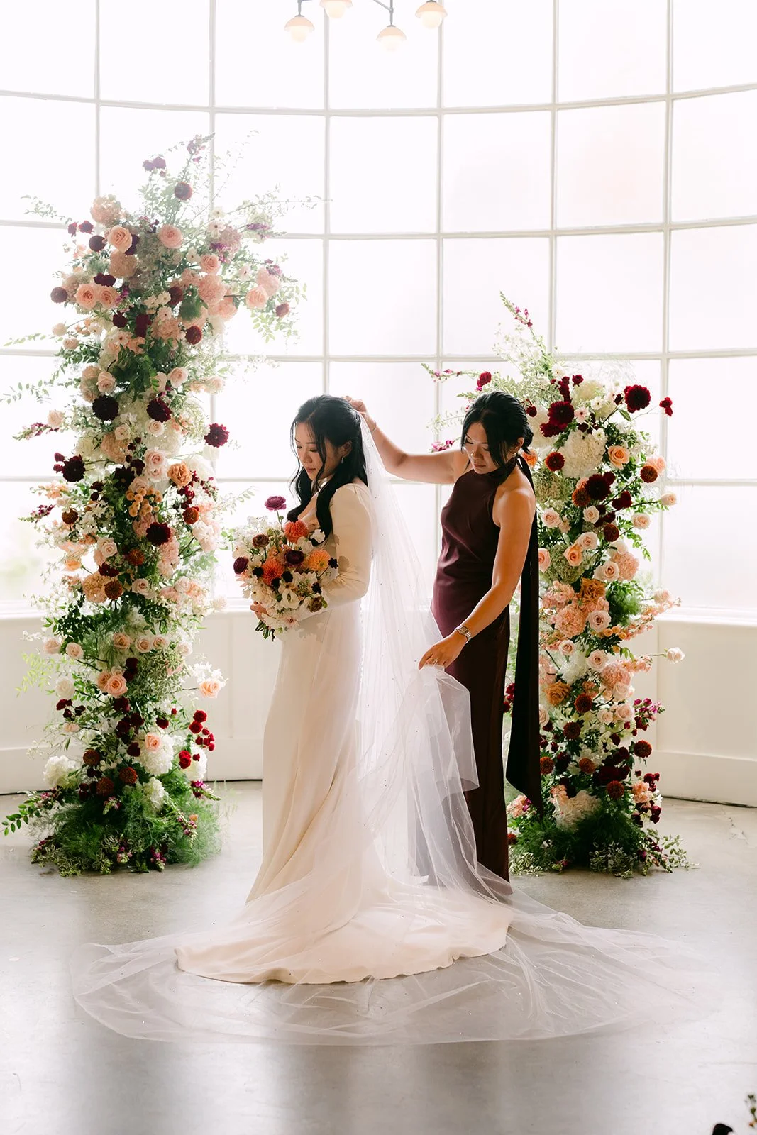 Denise's sister adjusting her veil between towering floral columns.