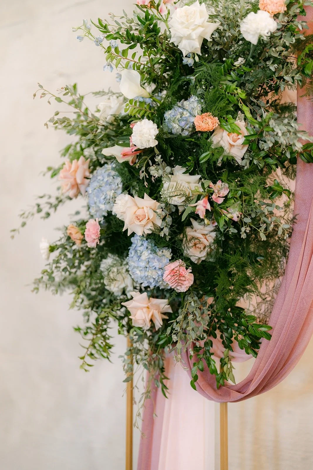 Blush, white and blue florals on the ceremony arch with pink draped fabric