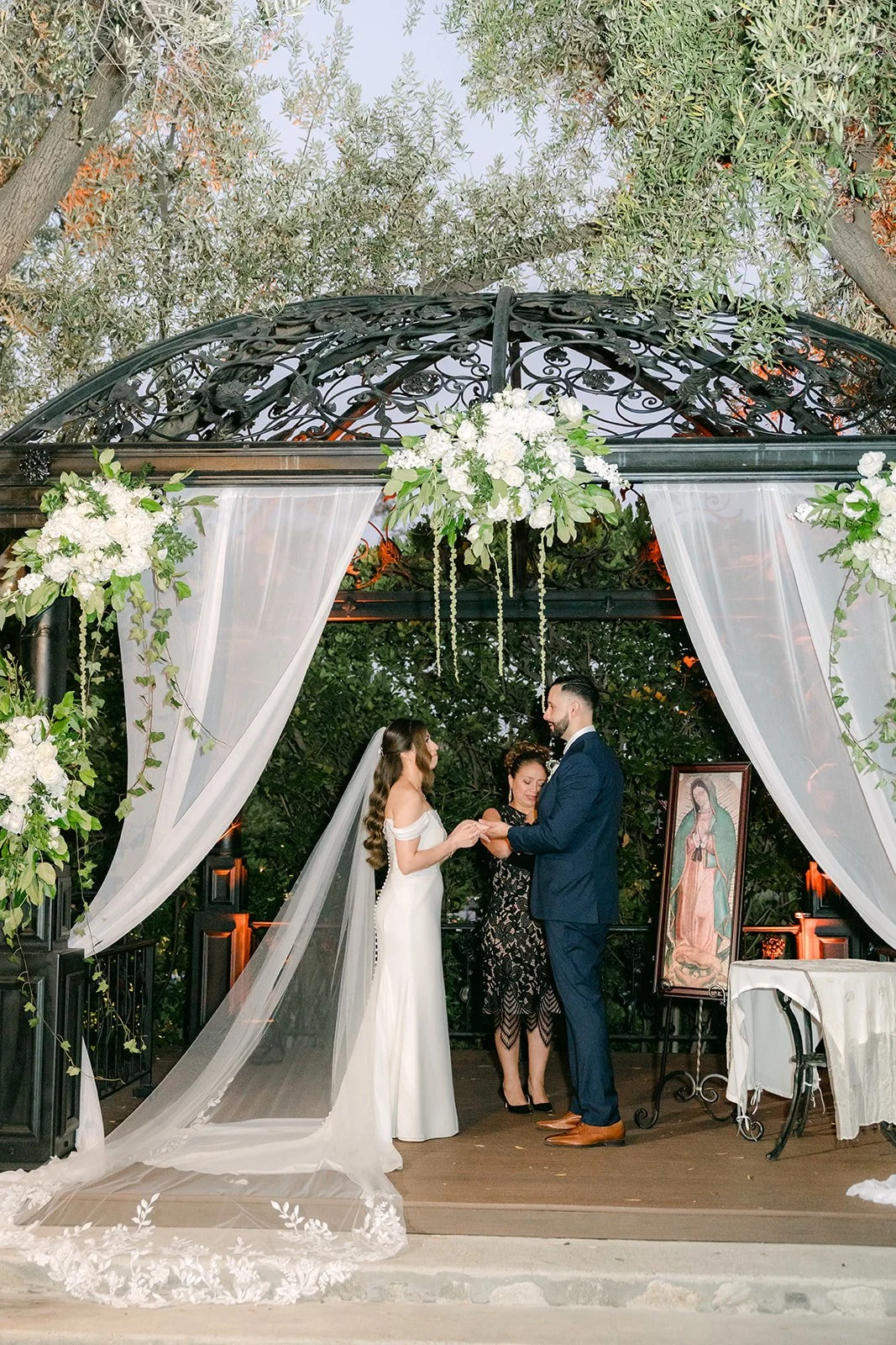 Wide view of the ceremony framed by the gazebo's white drapery and florals