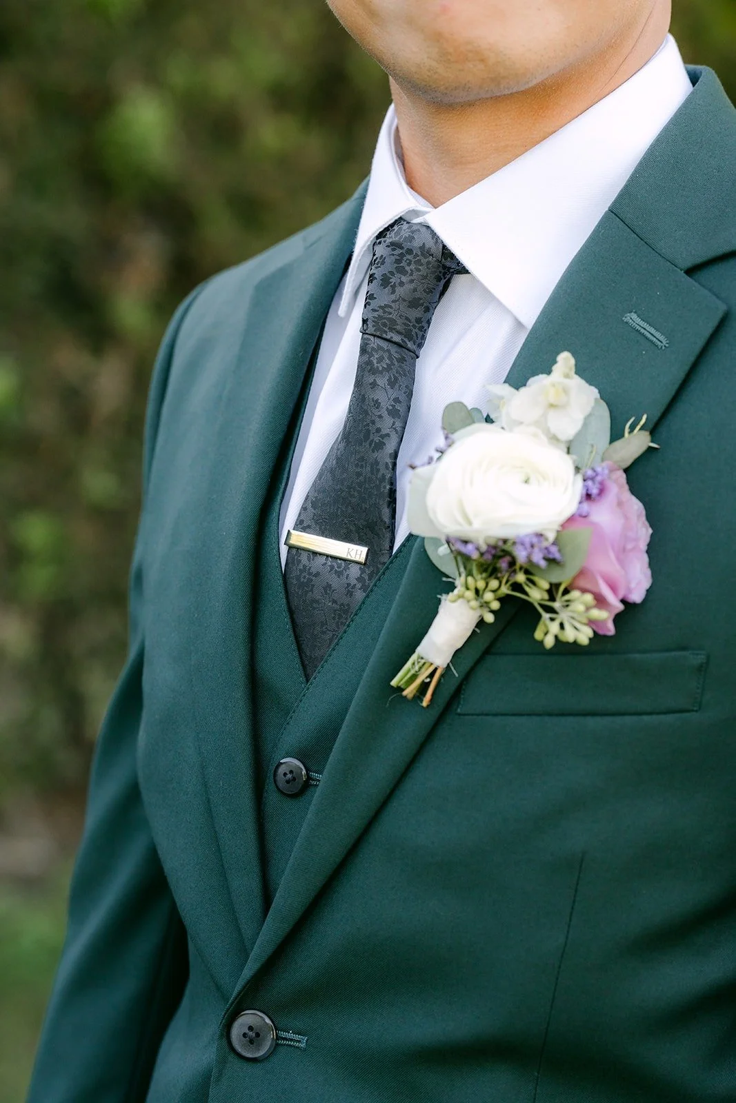 Kevin's boutonniere with a white and lavender bloom on his dark green lapel