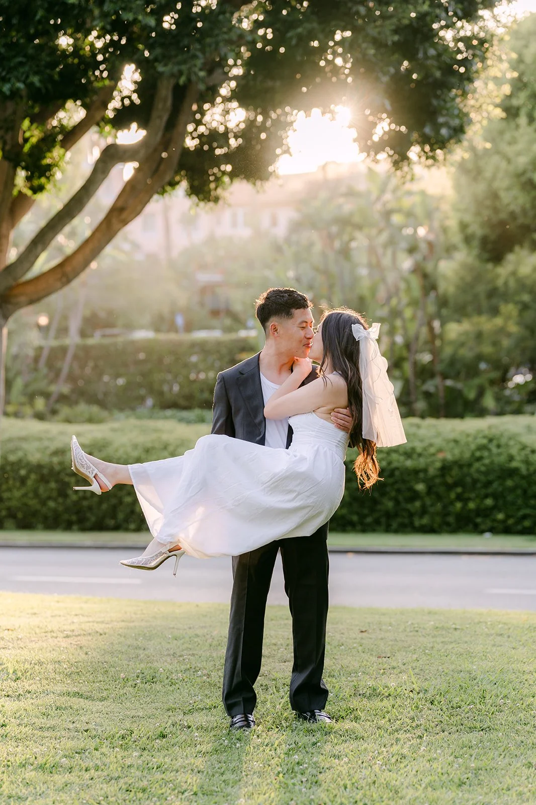 Richard carries Jadee in his arms on the lawn under the trees at golden hour.